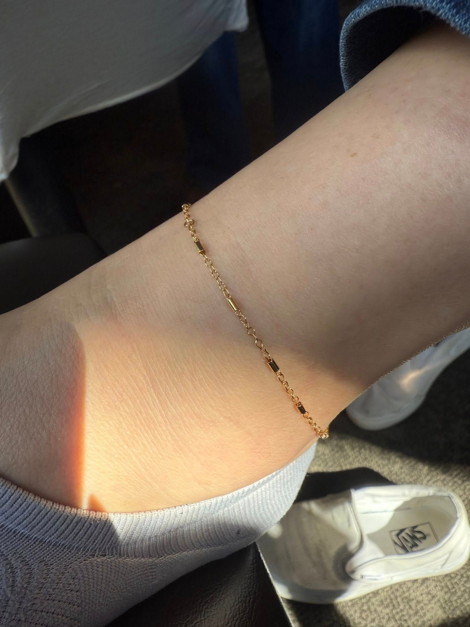 Leg with a delicate gold anklet in sunlight, wearing gray leggings and a white sneaker nearby