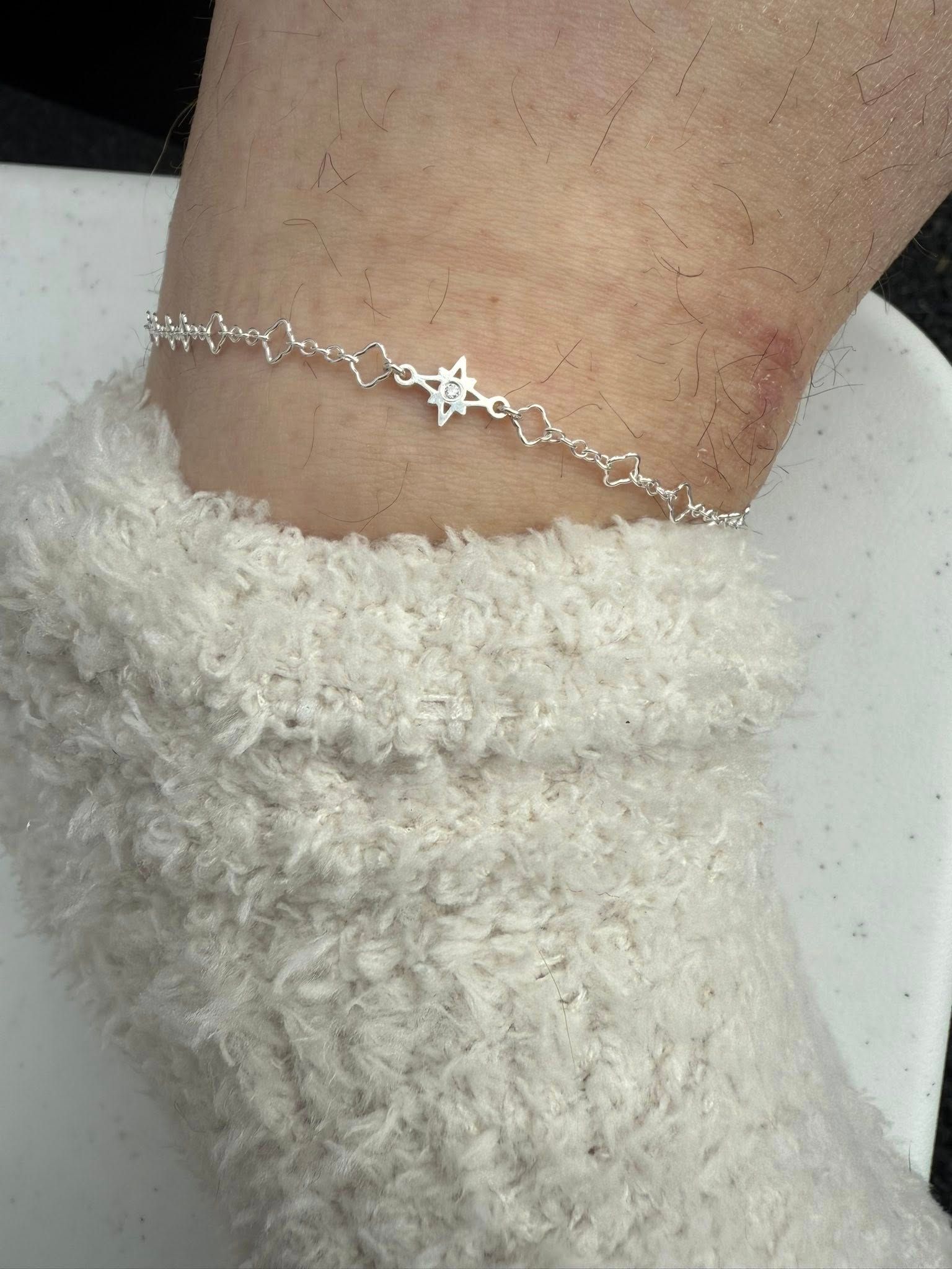 Close-up of an ankle with a delicate silver star anklet and fluffy white sock or leg warmer