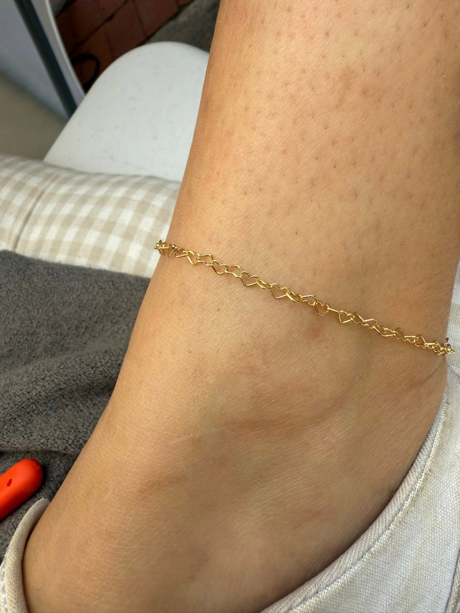Close-up of an ankle wearing a delicate gold chain bracelet on a light-colored couch