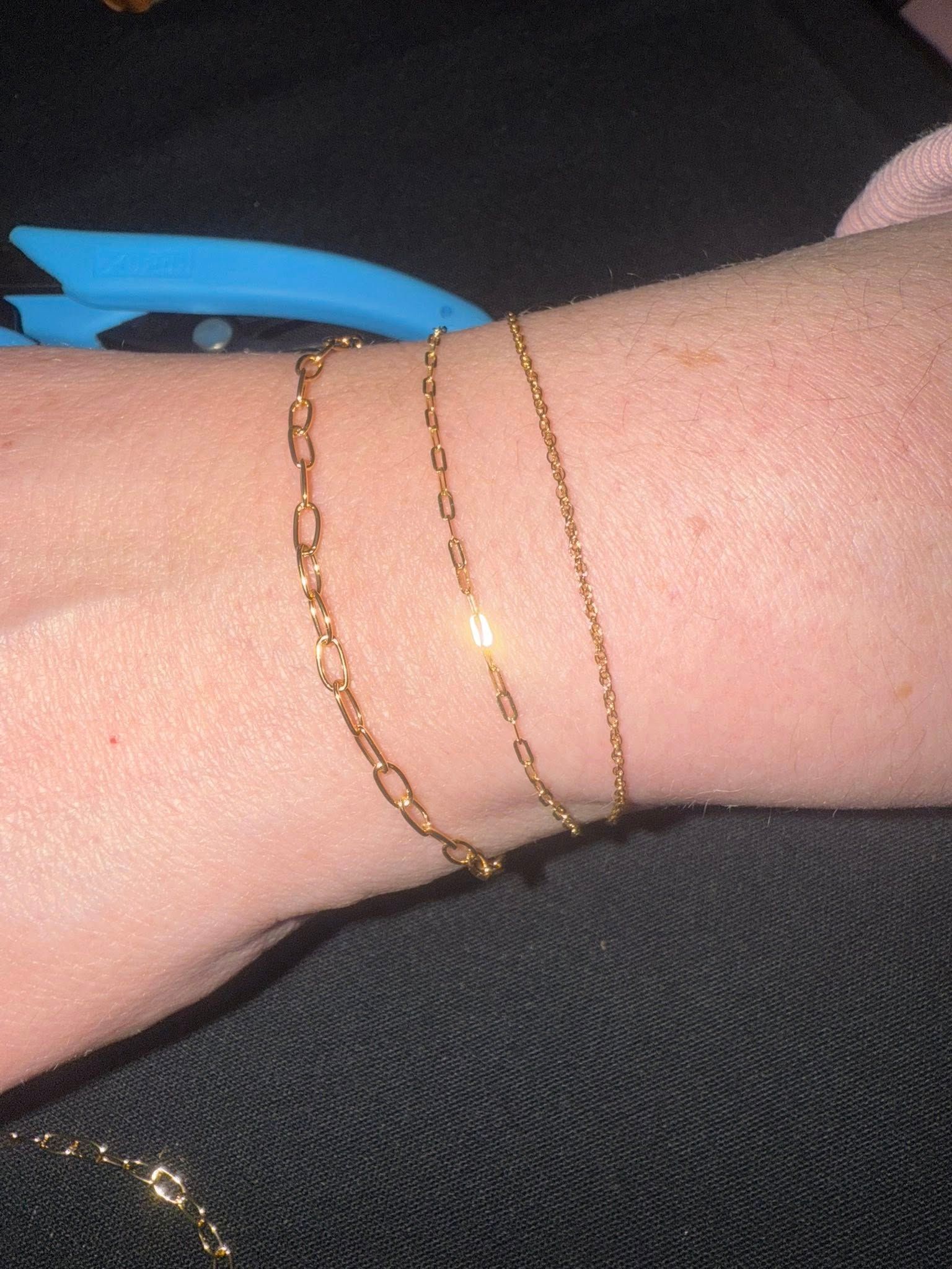 Wrist wearing two delicate gold chain bracelets on a light pink arm