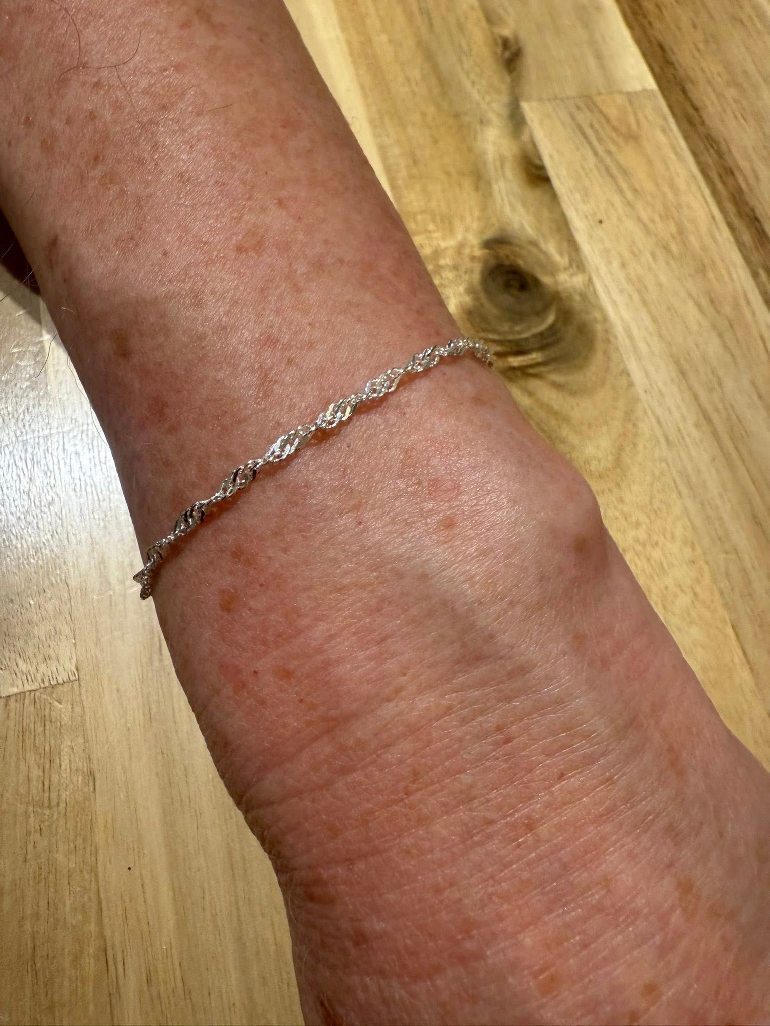 Close-up of a wrist wearing a thin silver bracelet on a wooden surface.