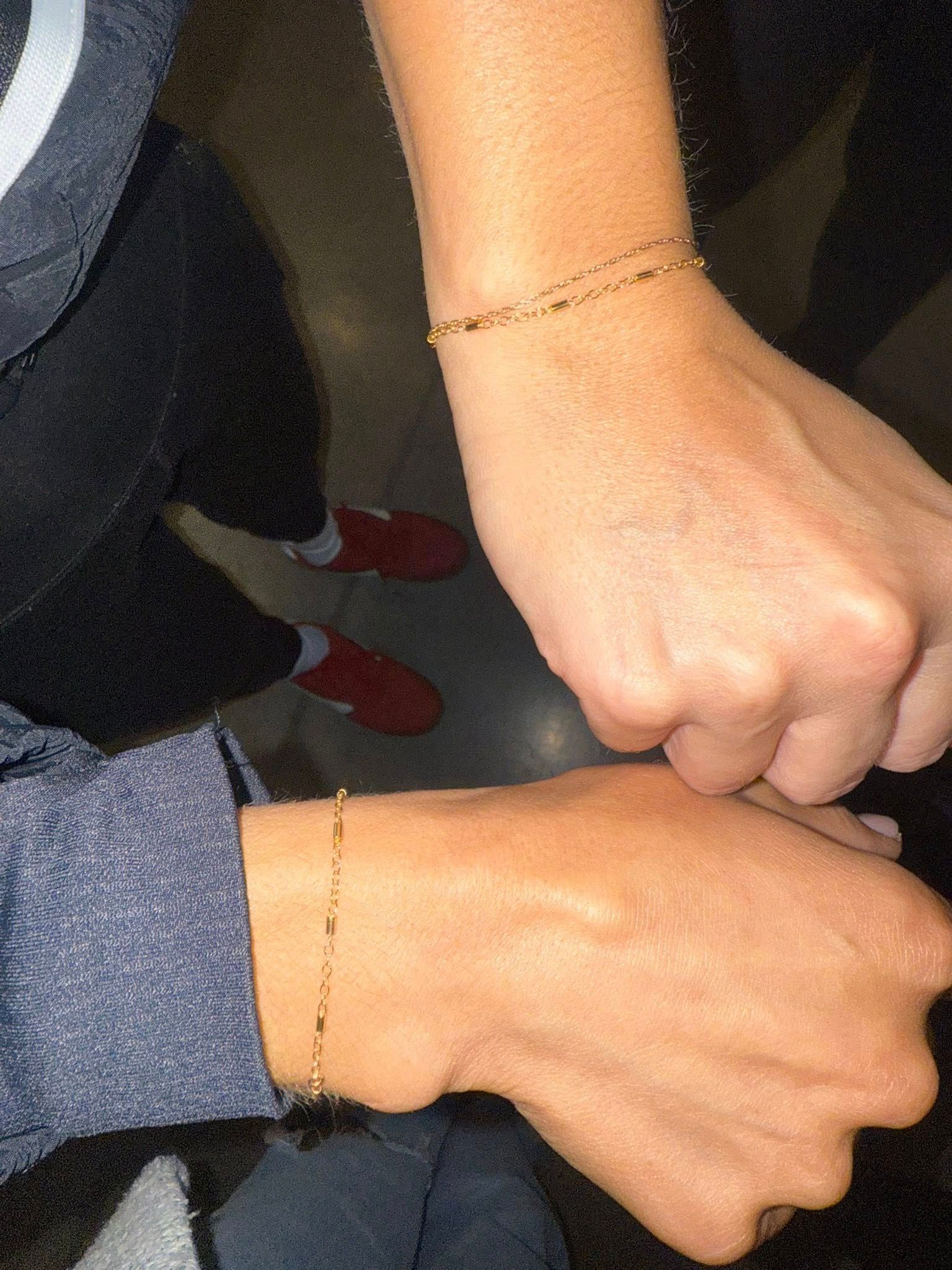 Two hands touching wrists, showing matching thin bracelet tattoos.