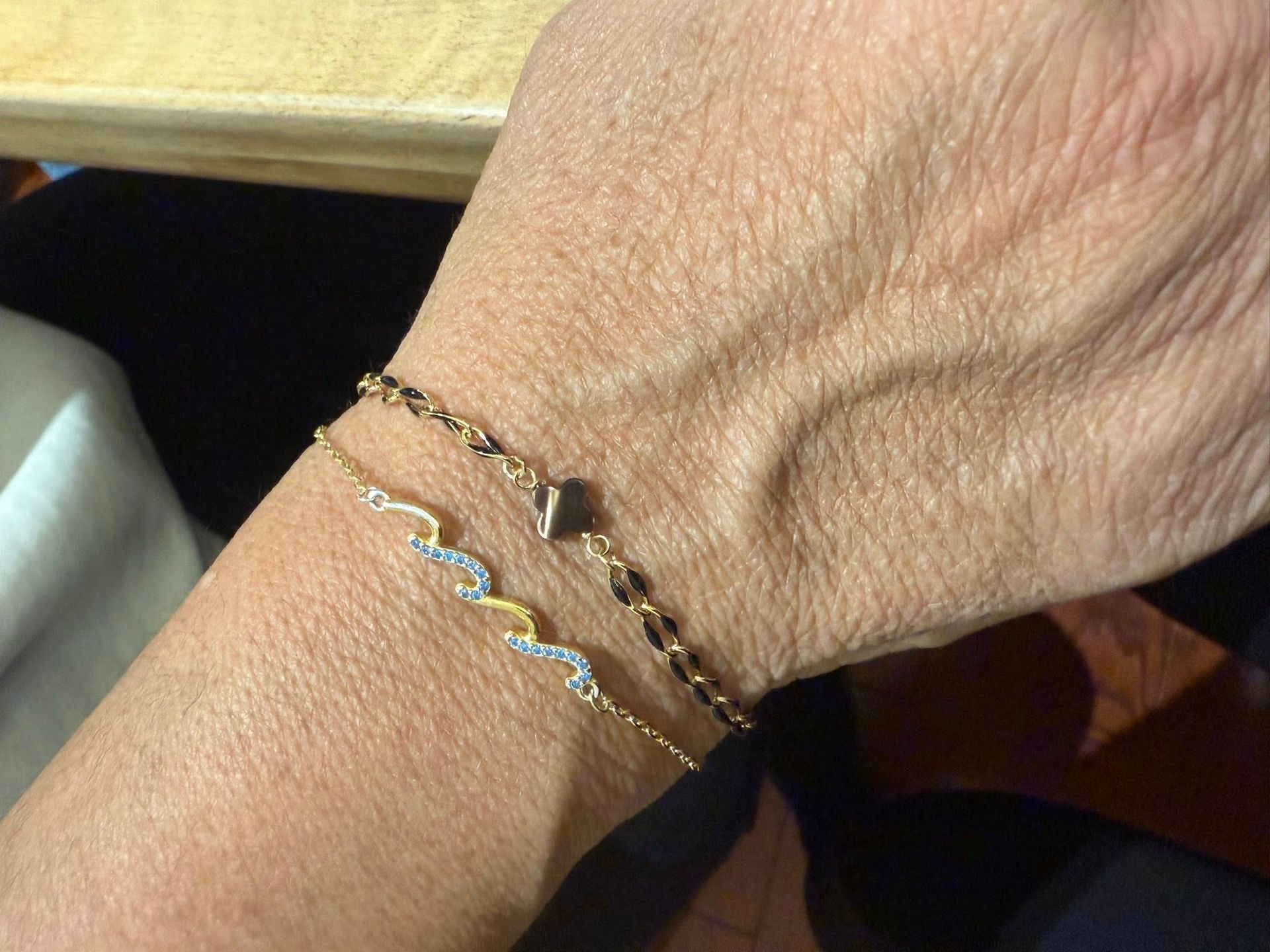 Close-up of a wrist wearing two delicate gold chain bracelets with small blue accents