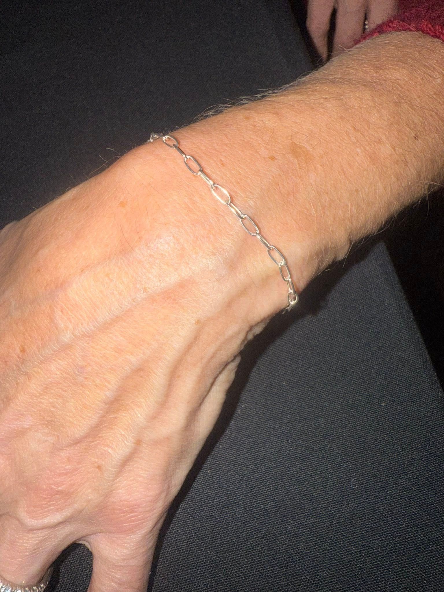 Close-up of a hand and wrist wearing a delicate silver bracelet against a dark background