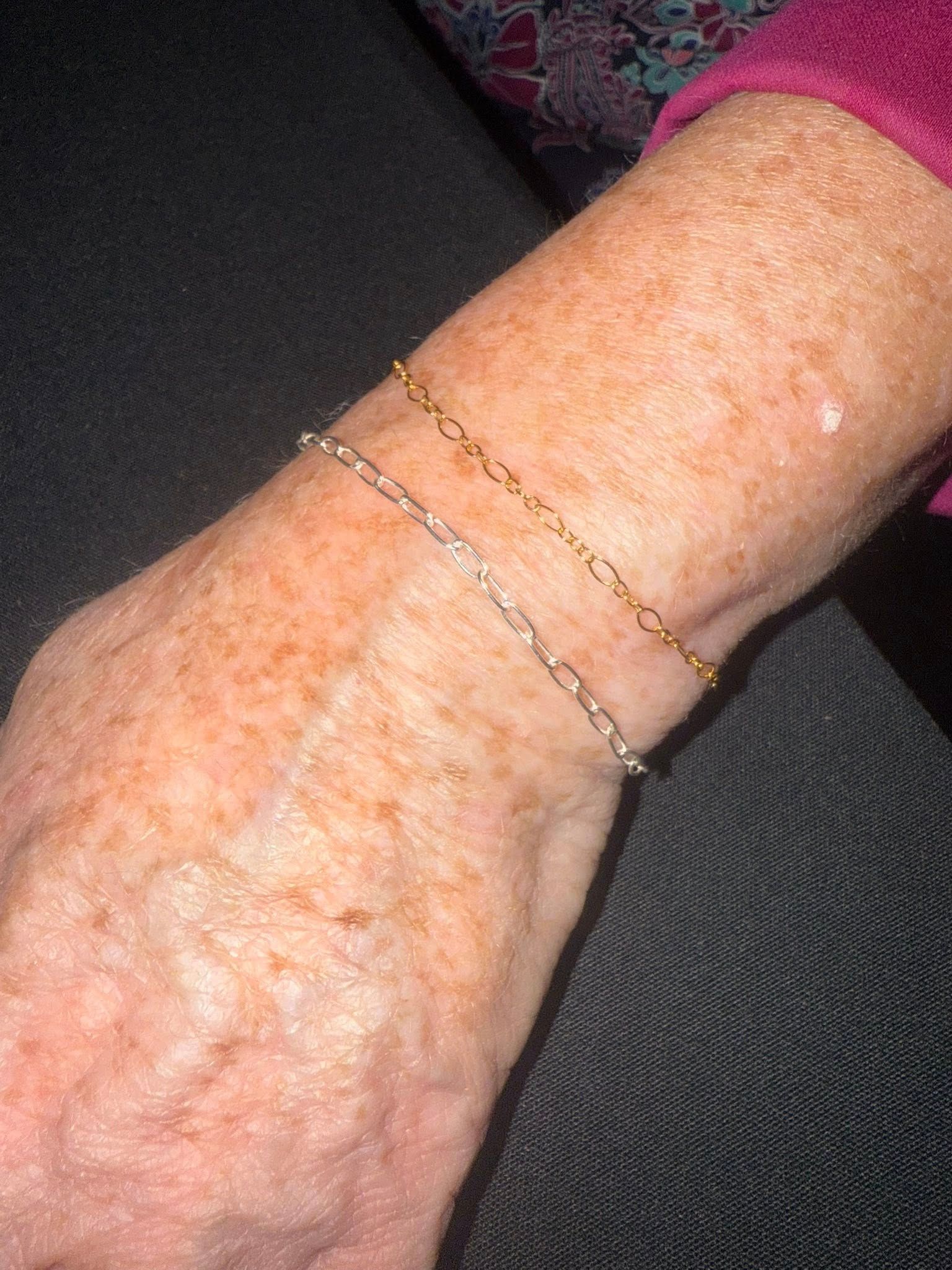 Close-up of a wrist and hand wearing two thin gold bracelets and a pink sleeve