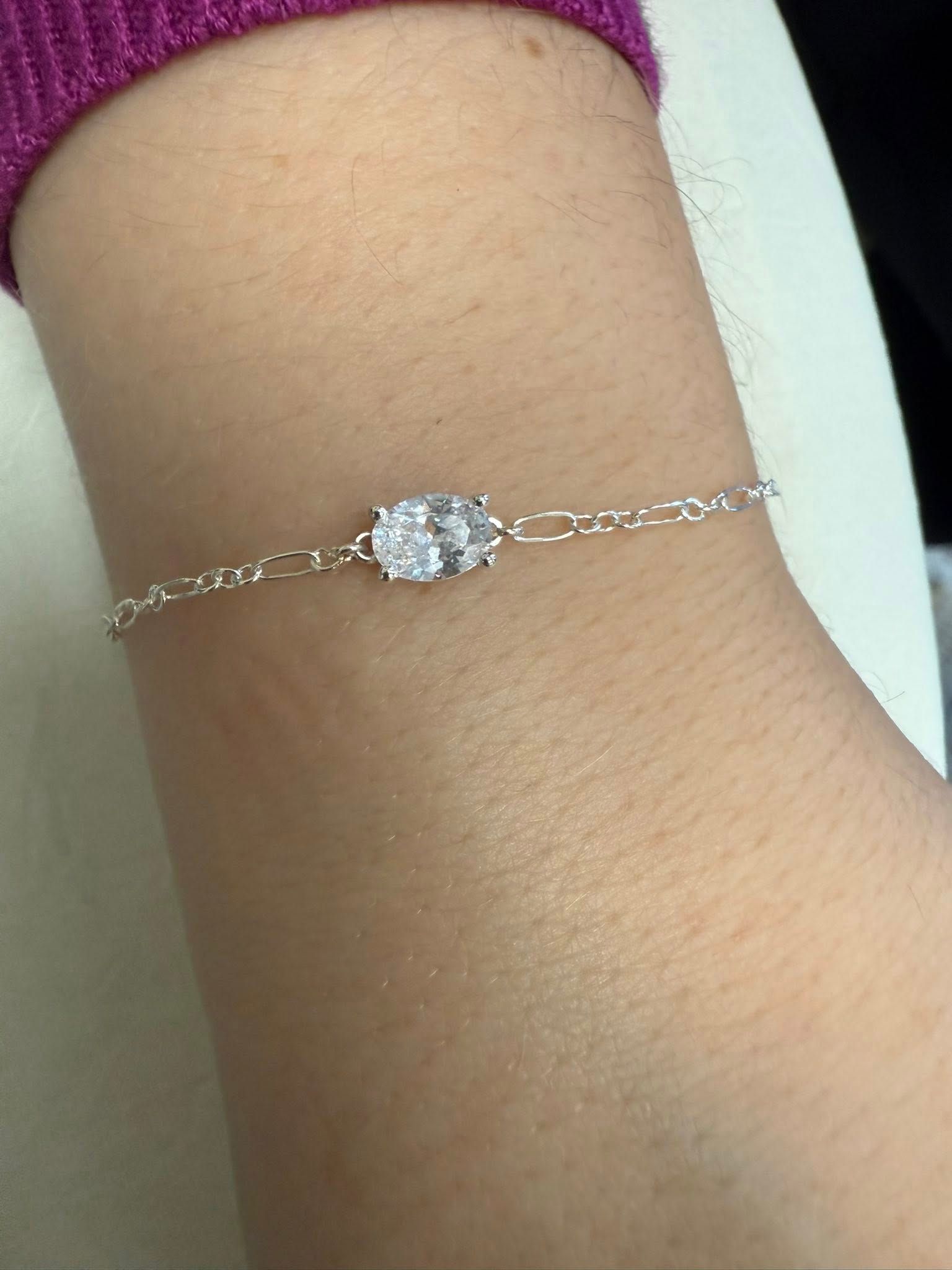 Close-up of a wrist wearing a delicate silver bracelet with a small oval pendant.