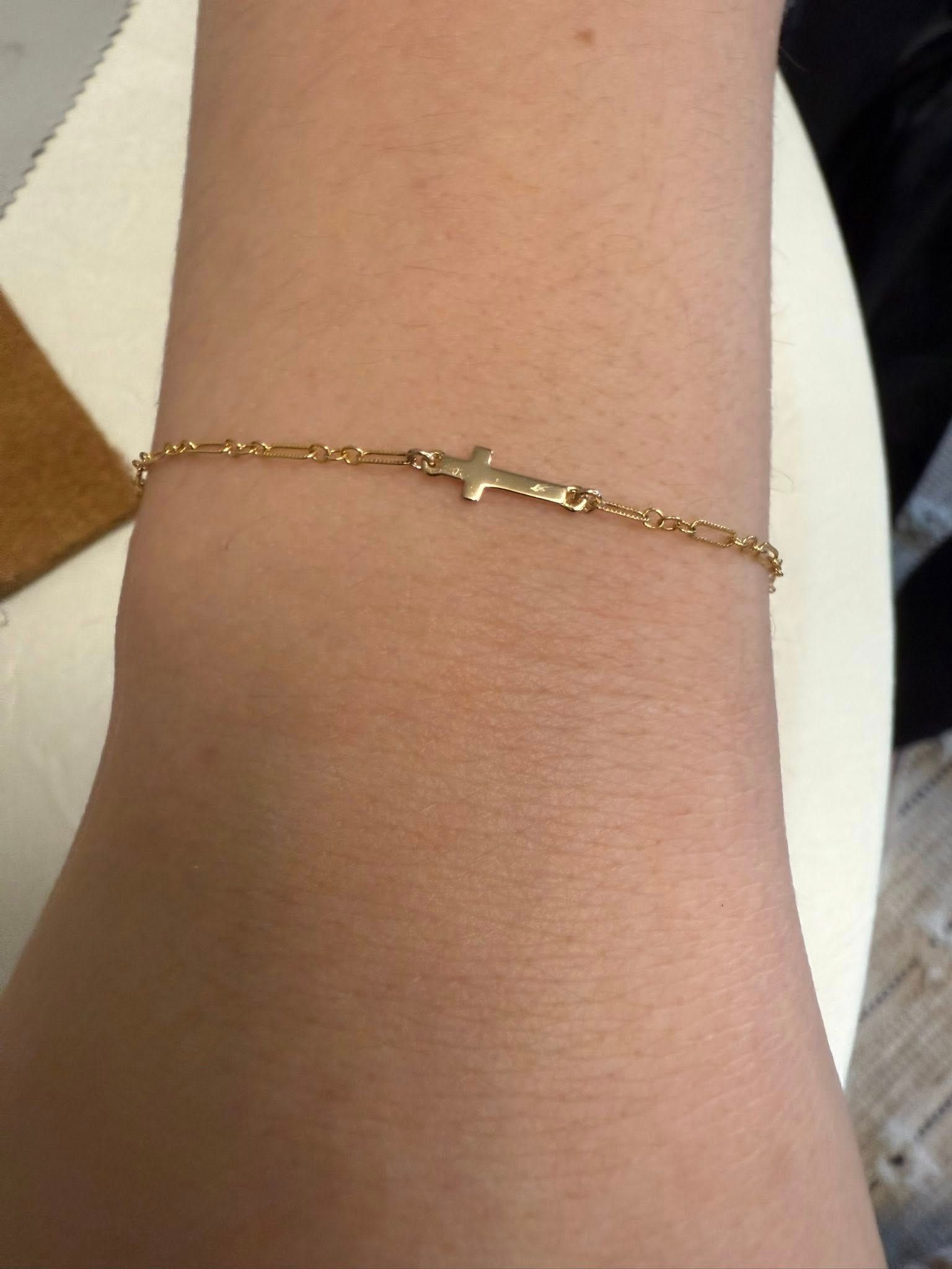 Gold chain bracelet on a wrist with a small central charm.