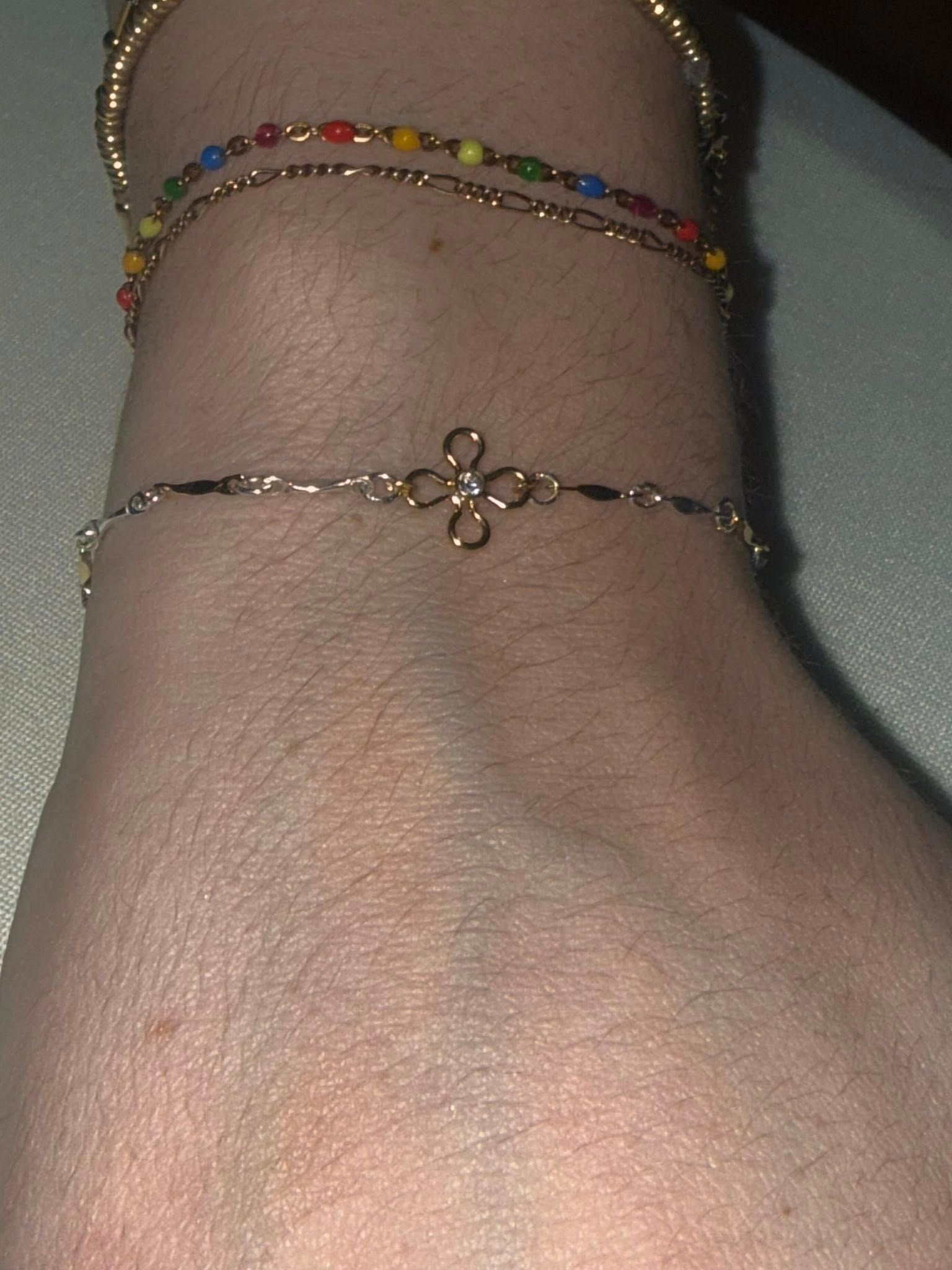 Ankle with two delicate bracelets, one gold chain with colorful beads and one thin gold flower charm bracelet.