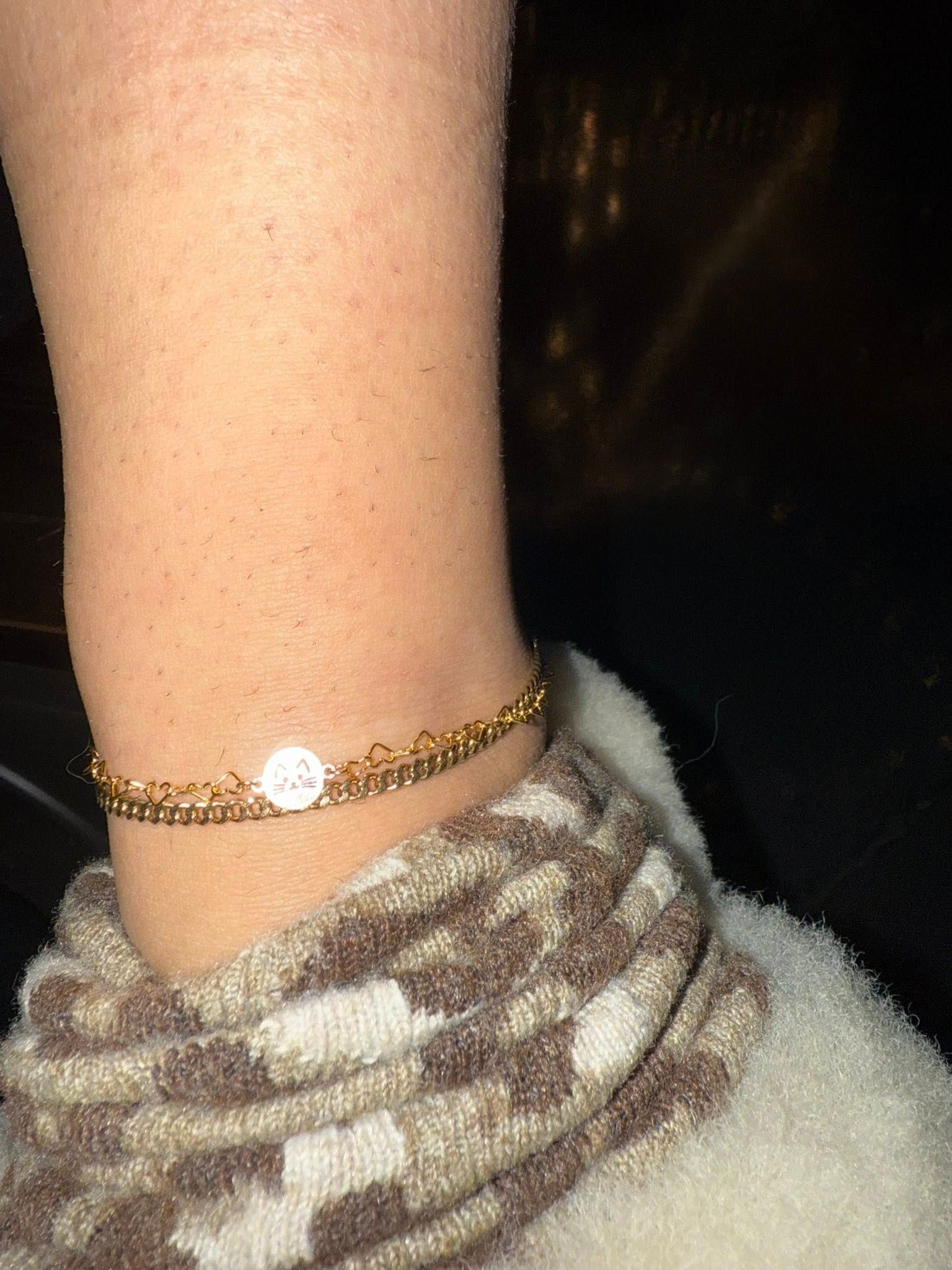Close-up of a bare ankle wearing a gold bracelet and a gray patterned sock