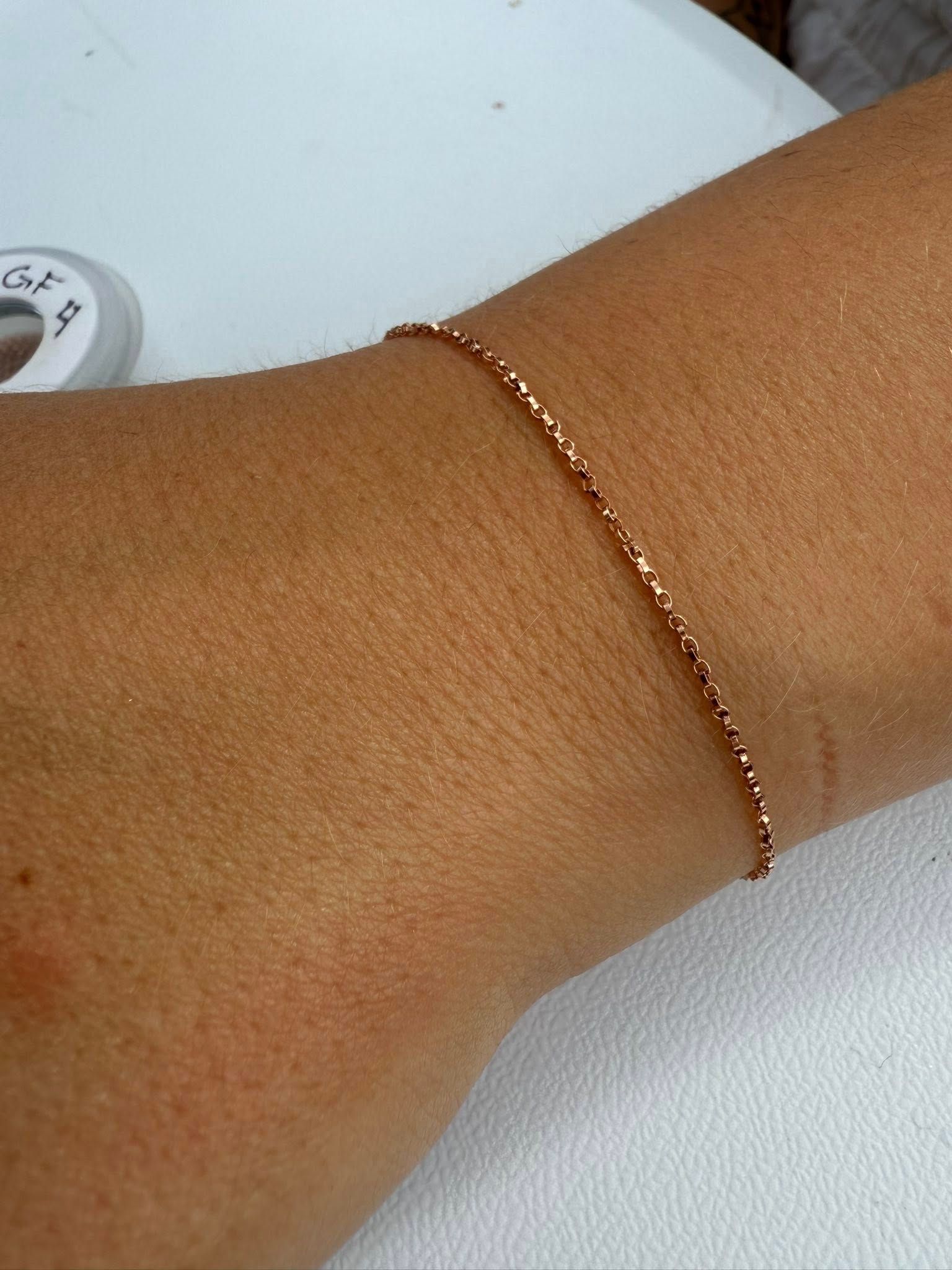 Close-up of a wrist wearing a thin rose gold bracelet on a white surface