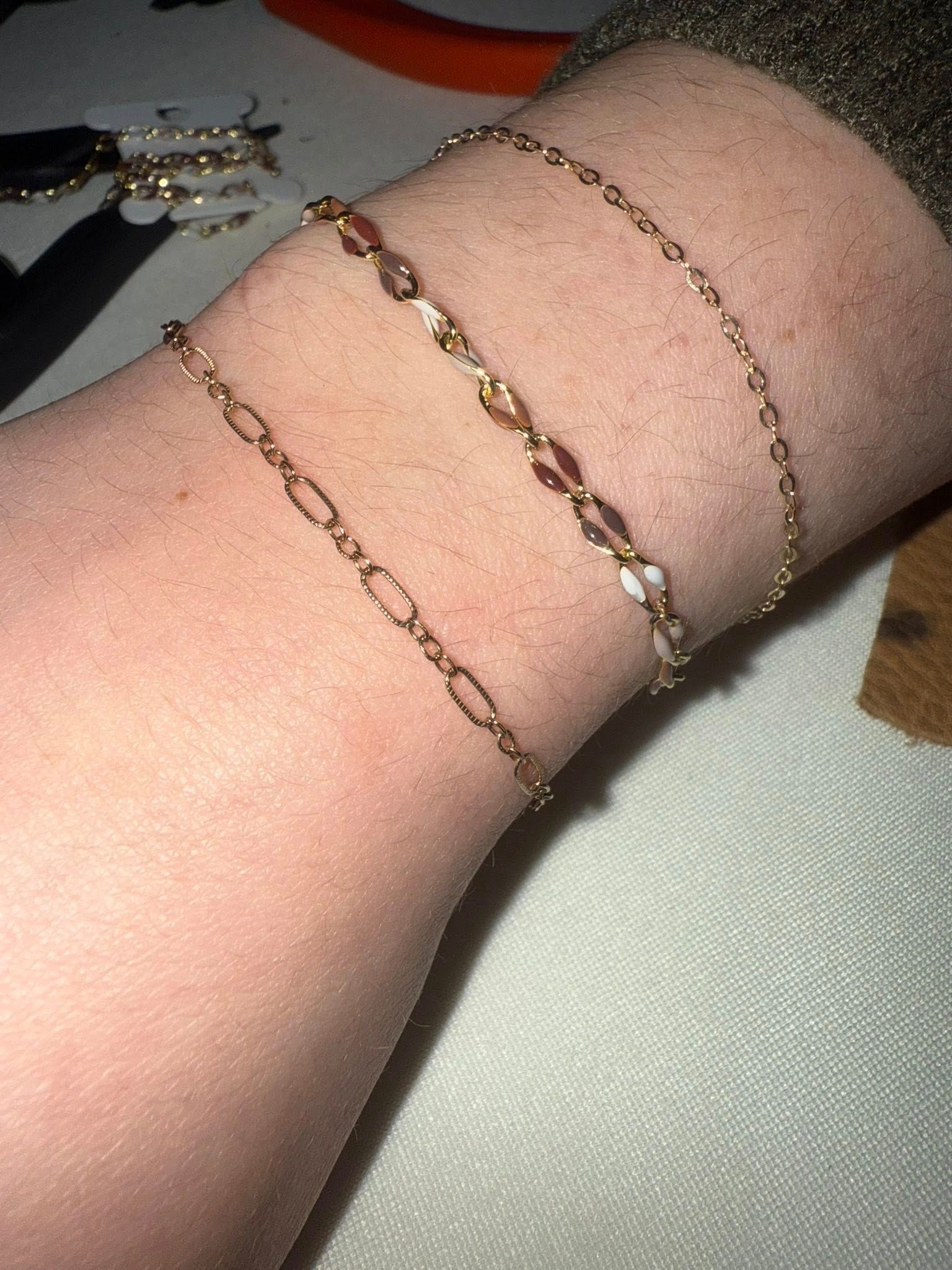 Two delicate gold bracelets on a person's wrist on a light fabric background