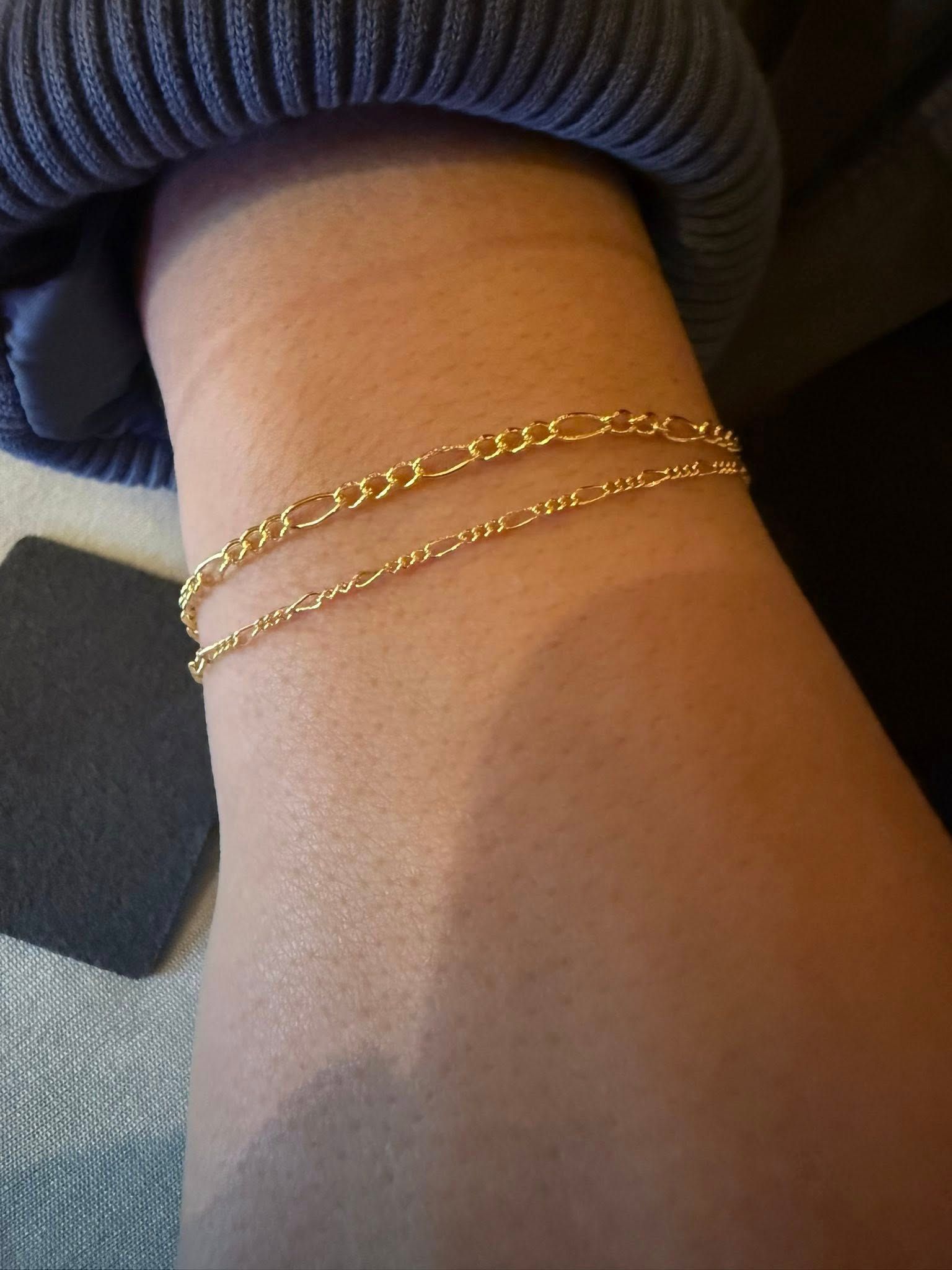 Close-up of a wrist wearing two thin gold chain bracelets.
