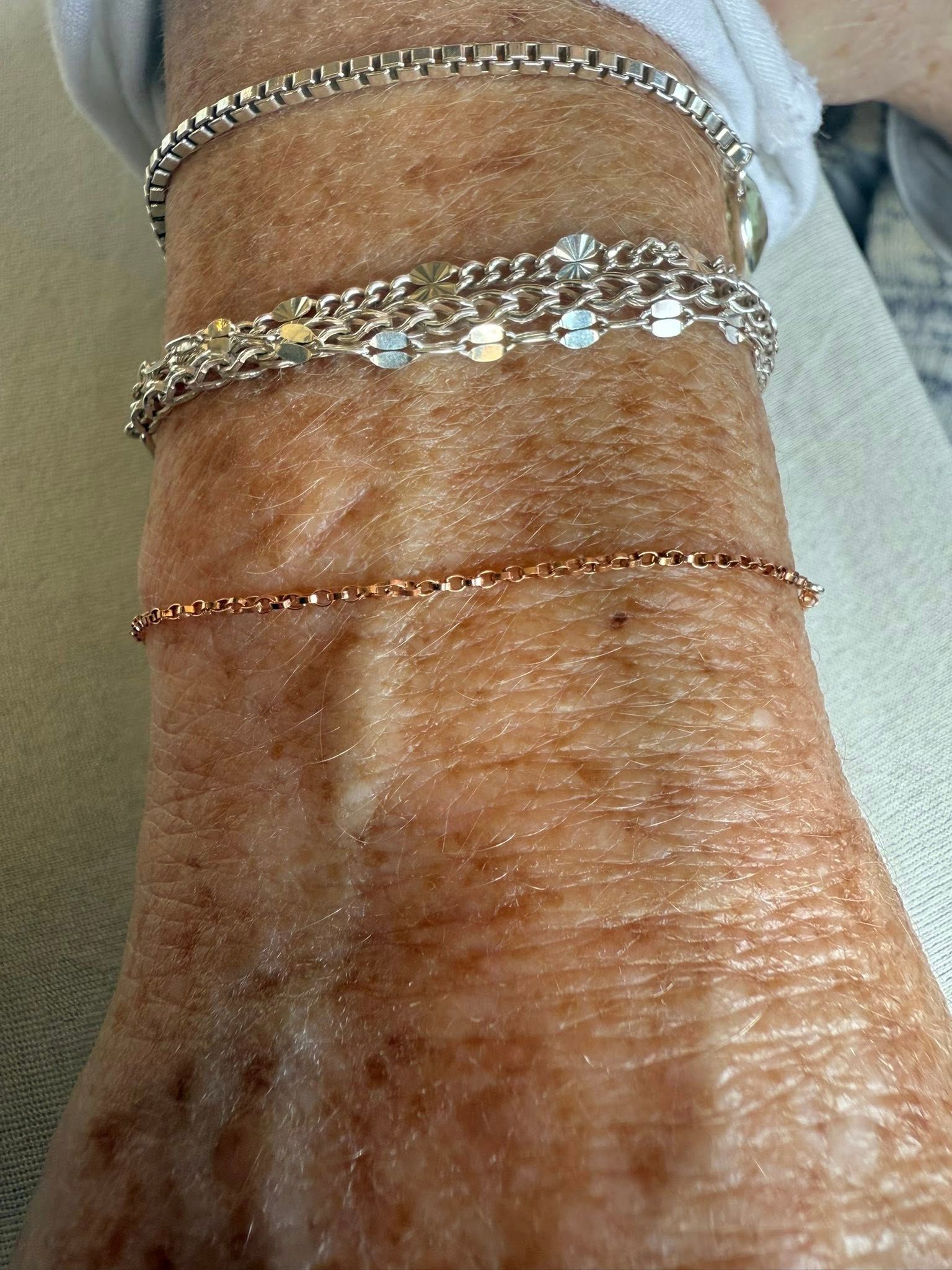 Close-up of a wrist wearing three silver bracelets and a thin rose-gold chain bracelet.