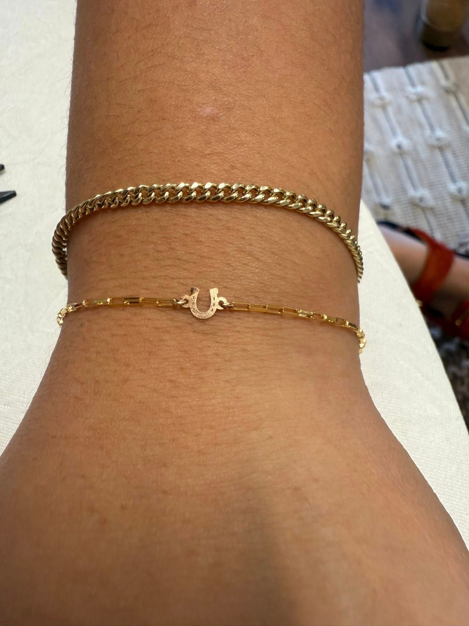 Close-up of an ankle wearing a gold chain bracelet and a thin gold anklet with a small charm.