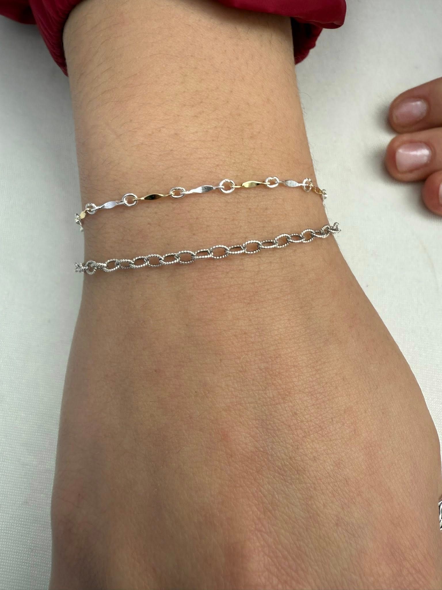 Close-up of a wrist wearing two thin silver chain bracelets