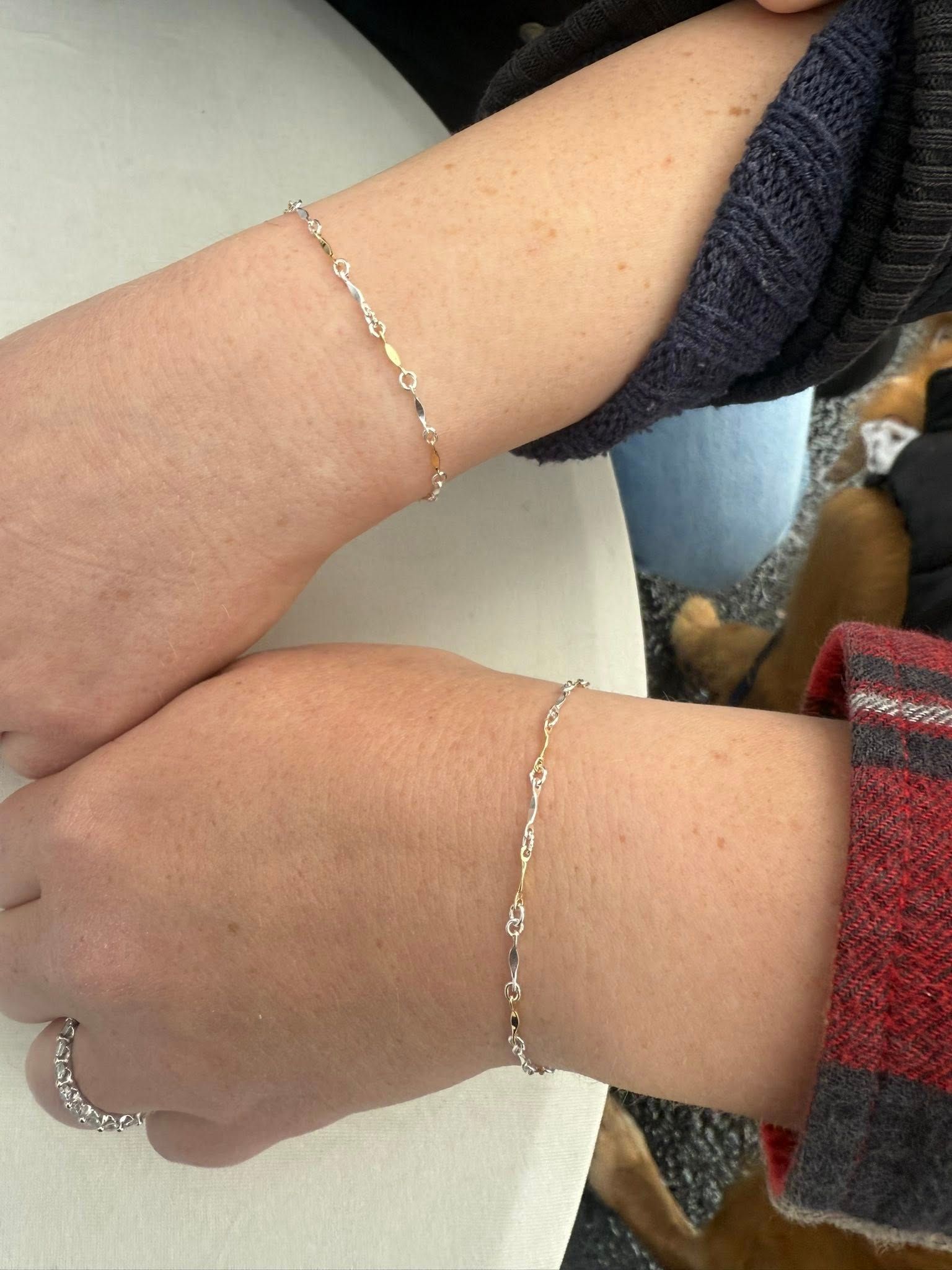 Two forearms with silver bracelets resting side by side on a white table.