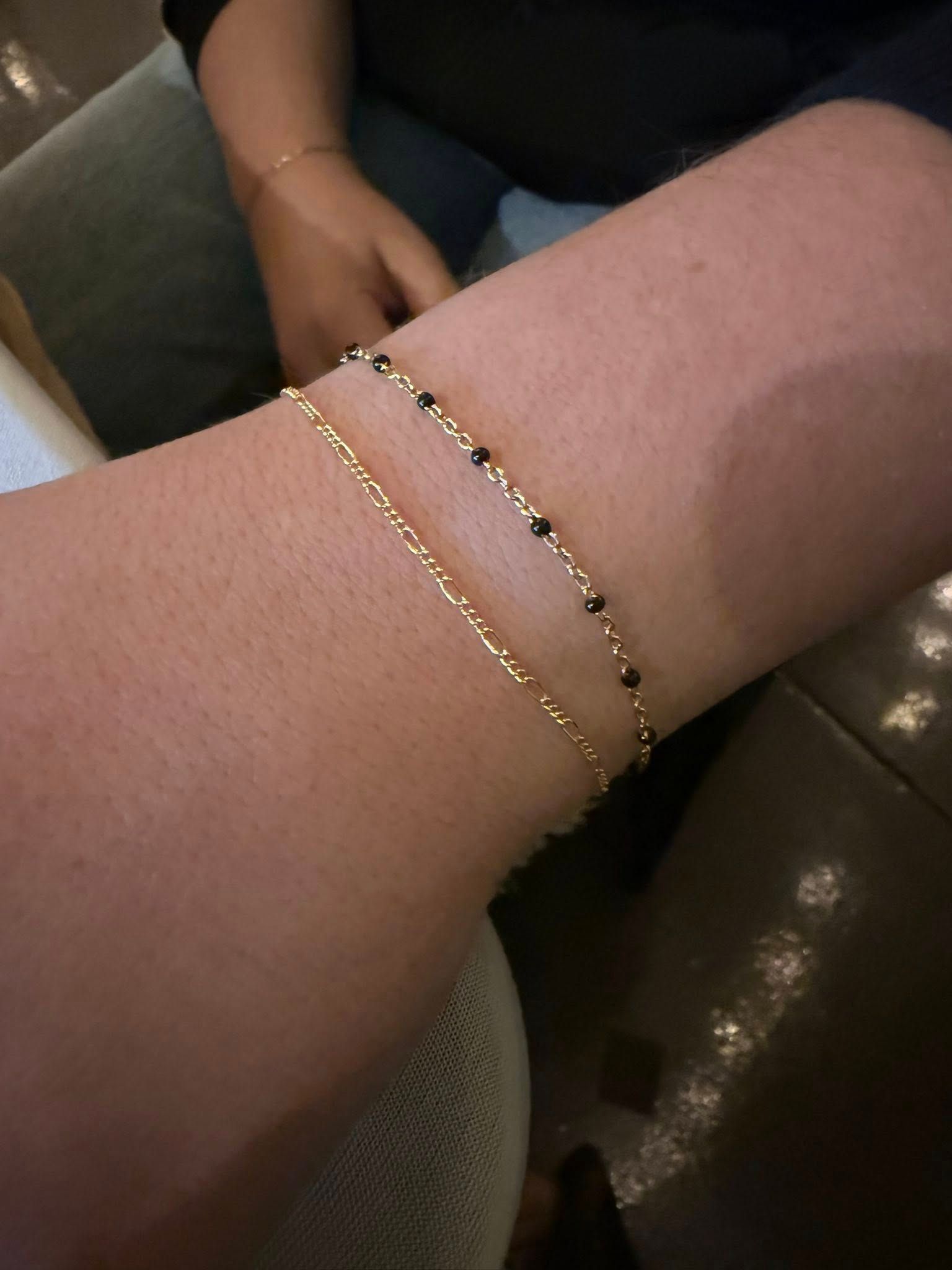 Close-up of a wrist wearing two delicate gold bracelets on a brown couch