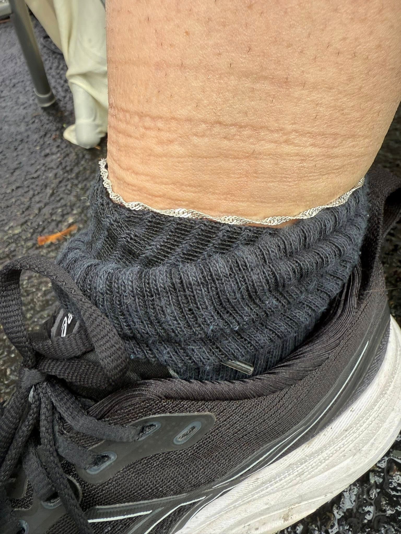 Close-up of a black sneaker and gray sock on a person's ankle, with a white pant cuff visible.