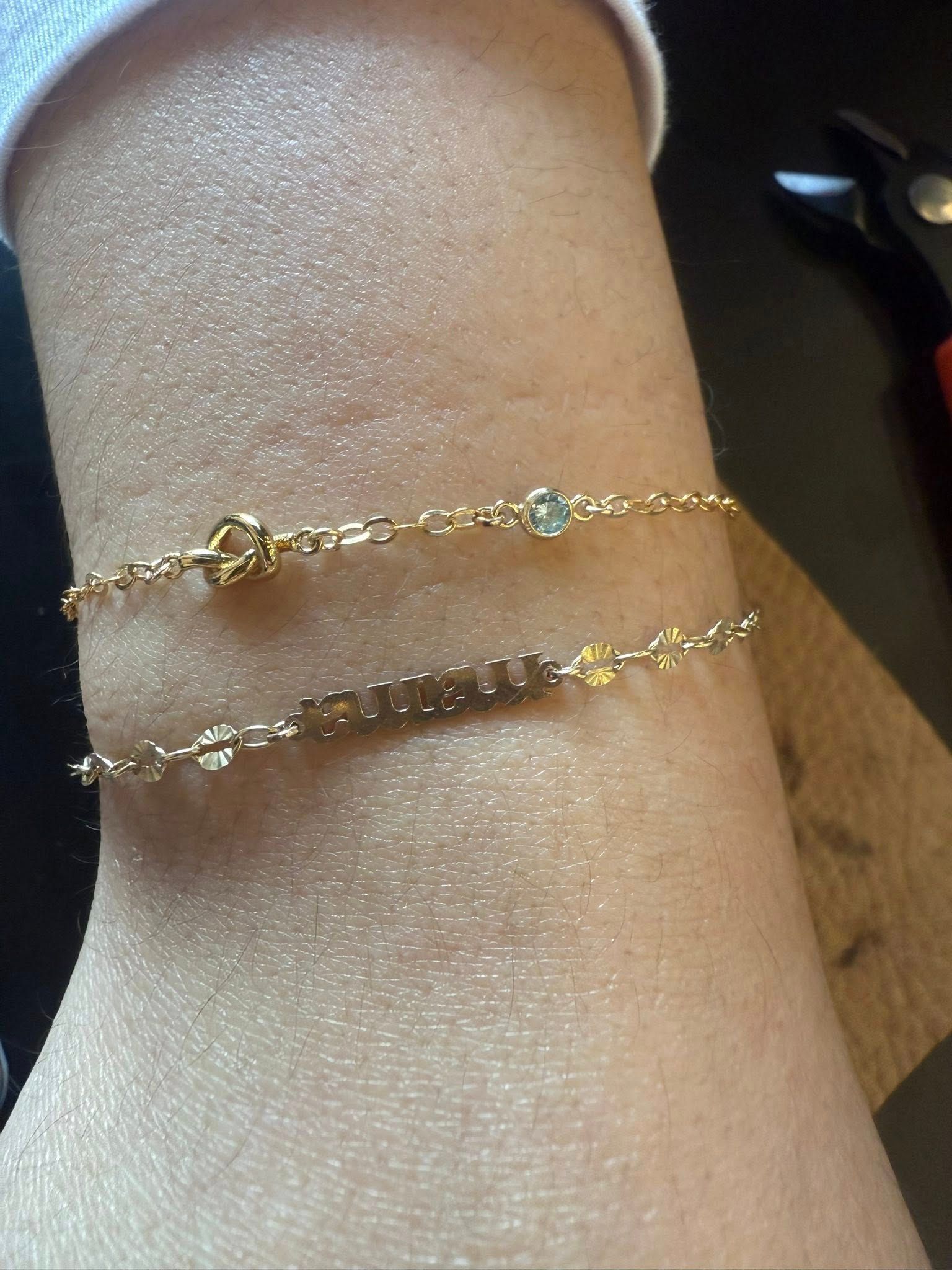 Two delicate gold bracelets stacked on a wrist, one with small charms and one with clear stones