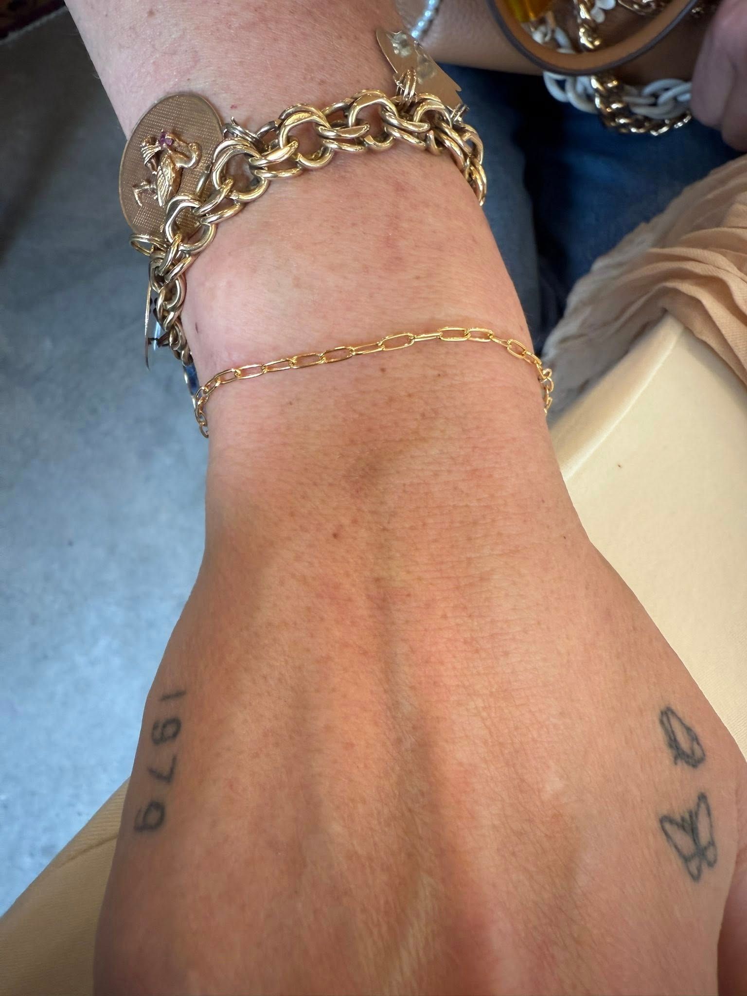 Close-up of a wrist with gold chain bracelets and small tattoos on the hand.