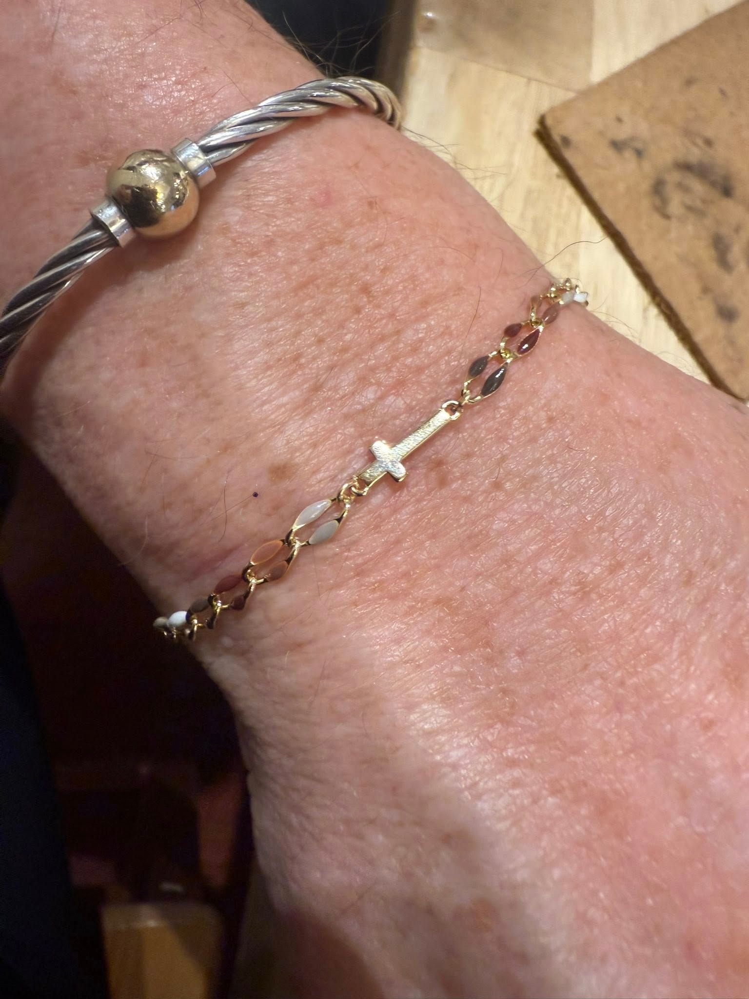 Two bracelets on a wrist: one silver braided bangle and one delicate gold chain with tiny charms