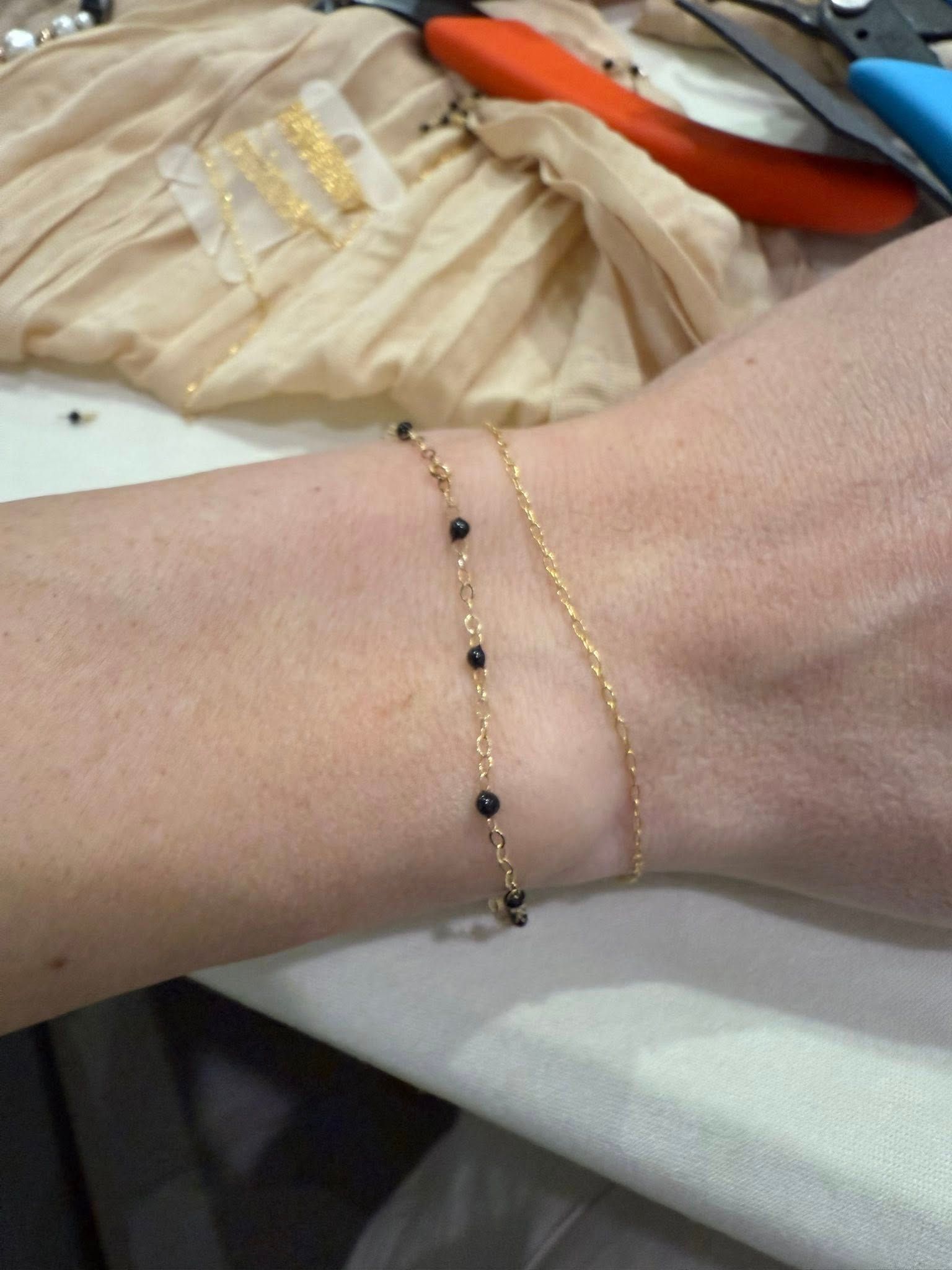 Close-up of a wrist wearing a black-beaded bracelet and thin gold bracelet on a white surface.