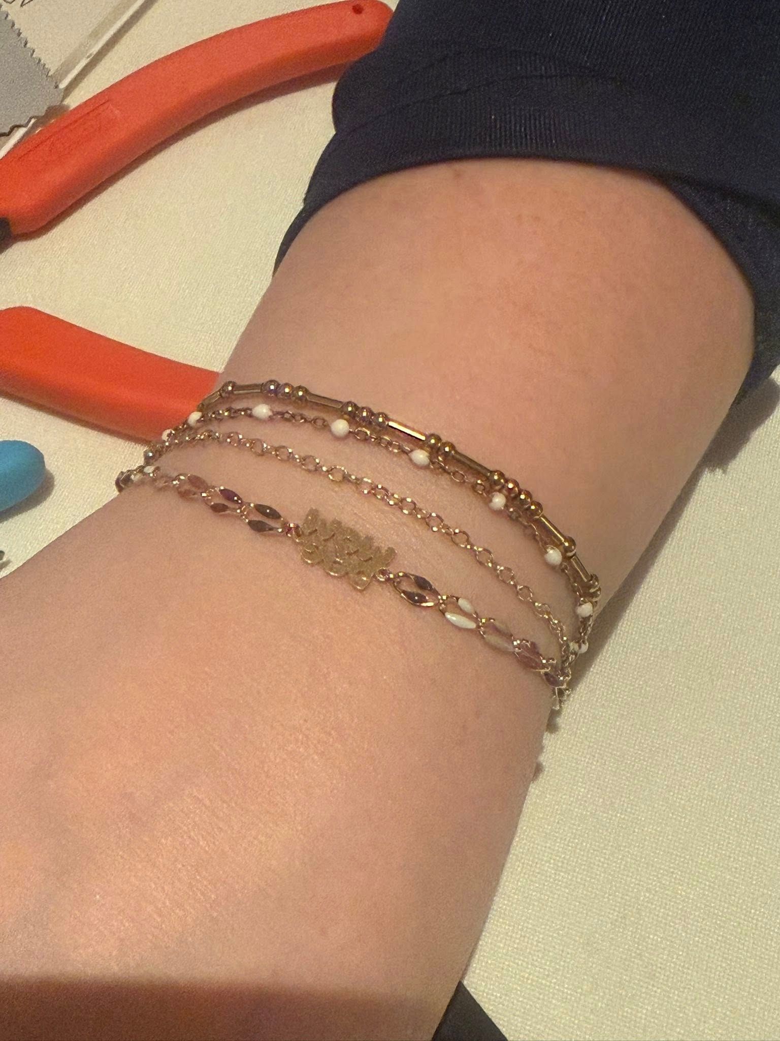 Close-up of an arm wearing three delicate beaded bracelets on a light background