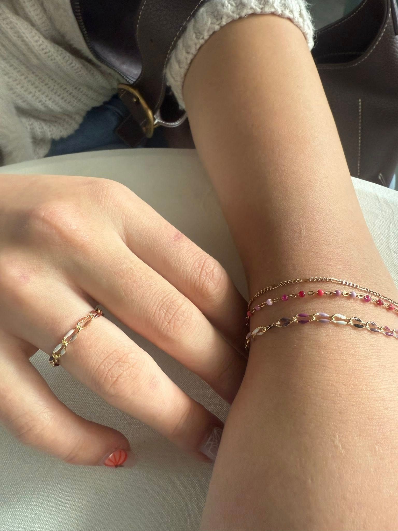 Hands with delicate beaded bracelets resting on a light-colored surface.