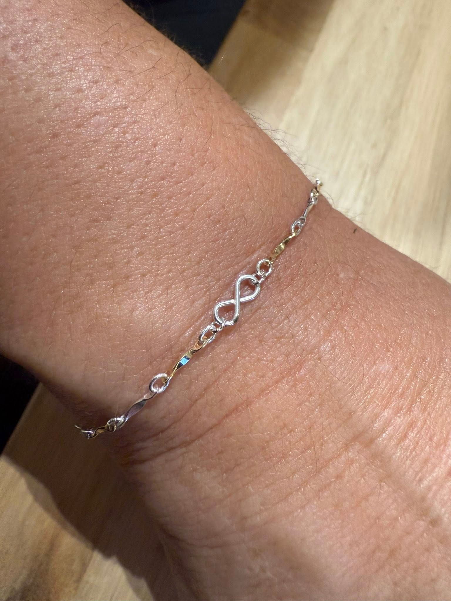 Close-up of a wrist wearing a delicate silver bracelet with heart-shaped links