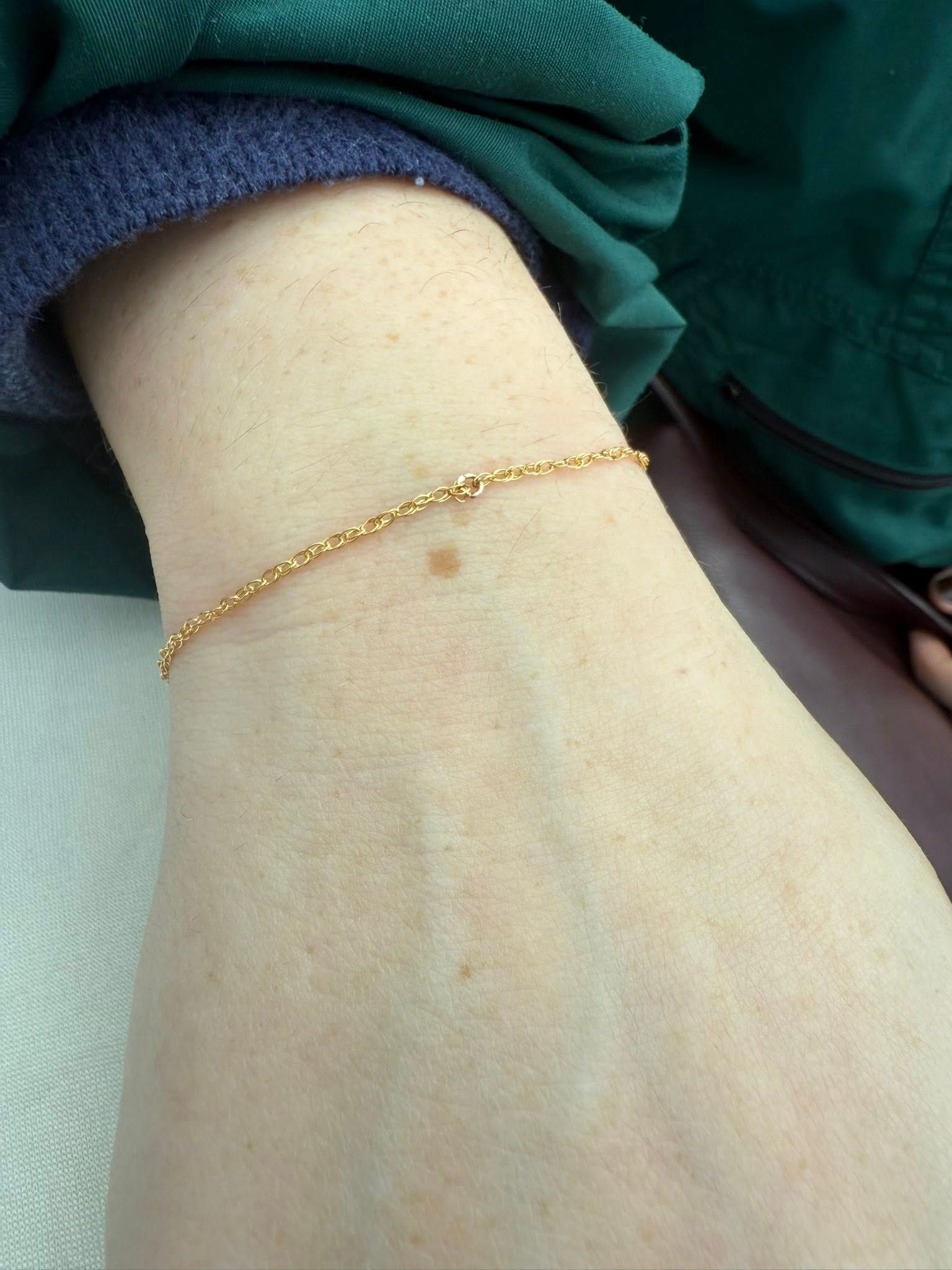 Close-up of a wrist wearing a thin gold bracelet against a green sleeve.