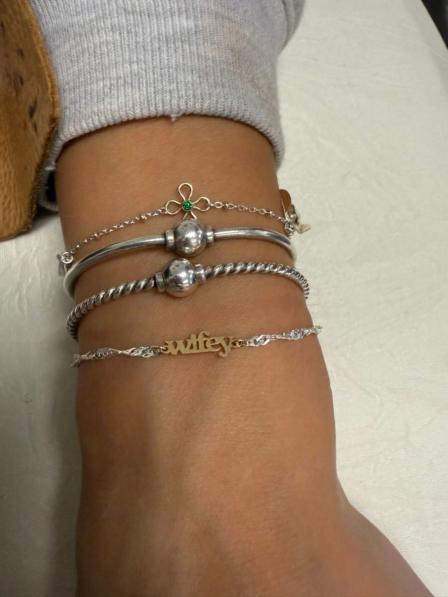 Ankle wearing layered silver and gold charm bracelets against a light background