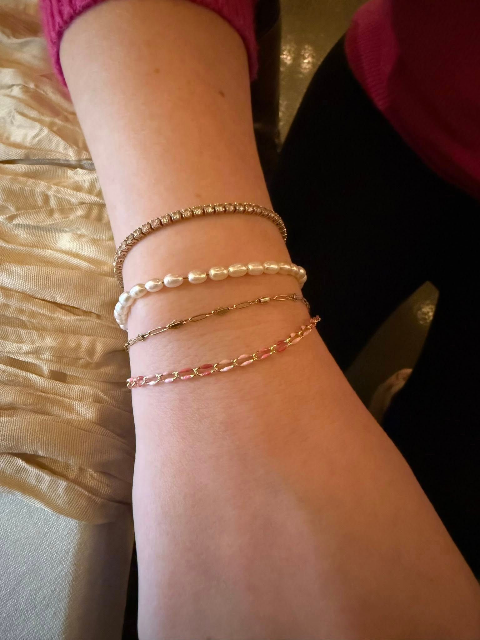 Close-up of a wrist wearing three delicate gold bracelets on a cream fabric background