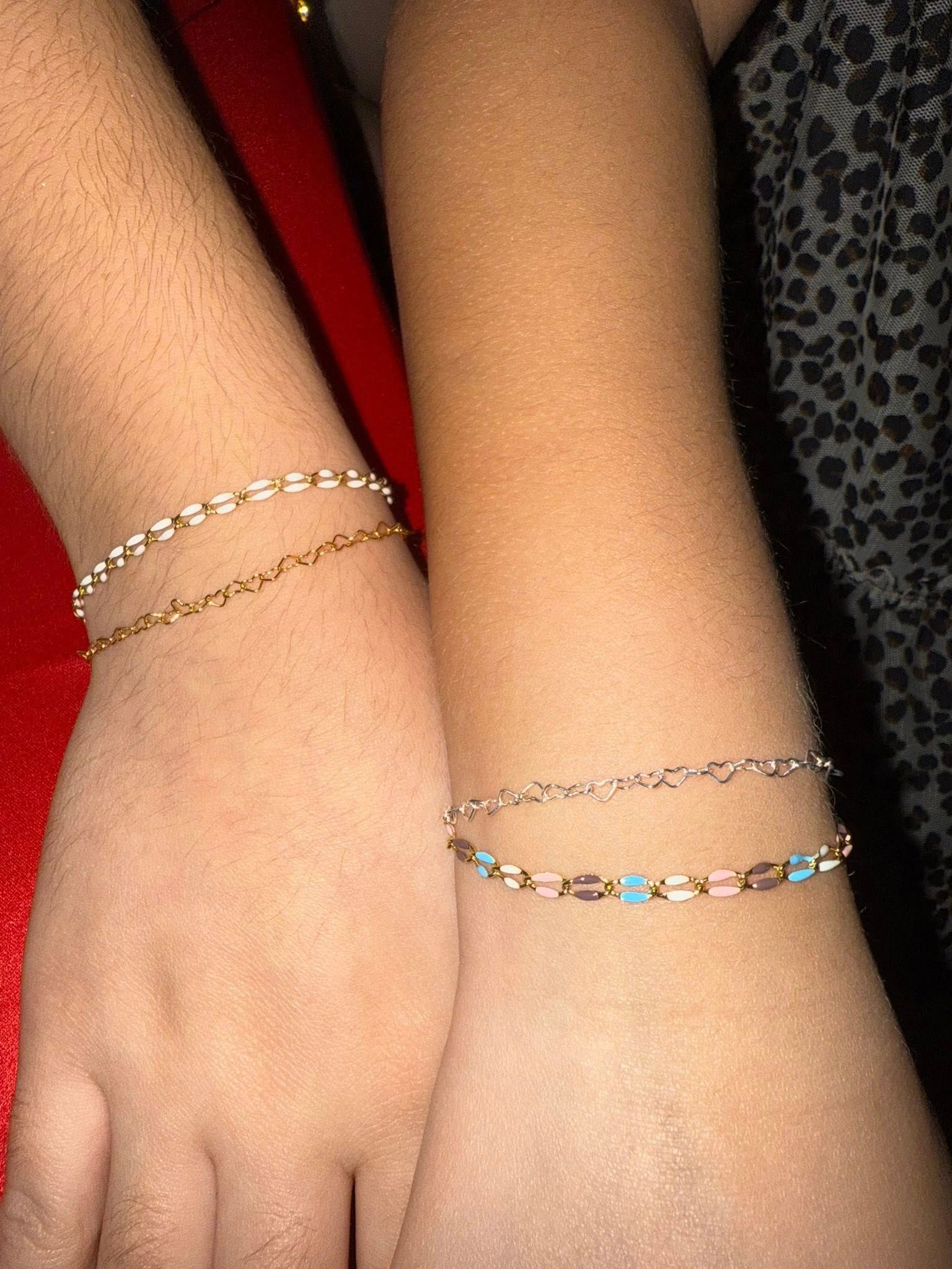 Two wrists wearing delicate silver bracelets on a red and black background