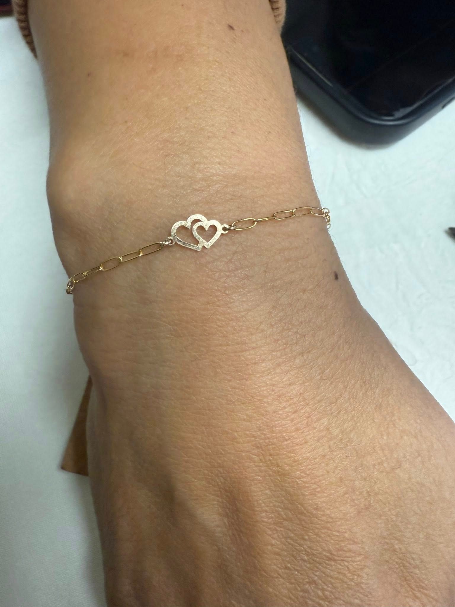 Close-up of a wrist wearing a delicate gold heart bracelet.