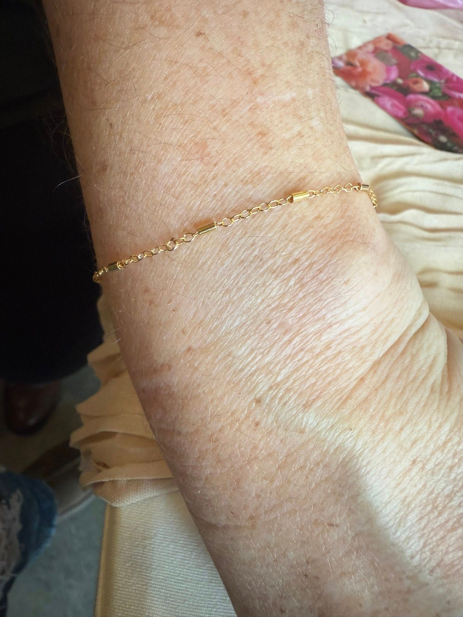 Close-up of a wrist wearing a thin gold chain bracelet on light fabric.