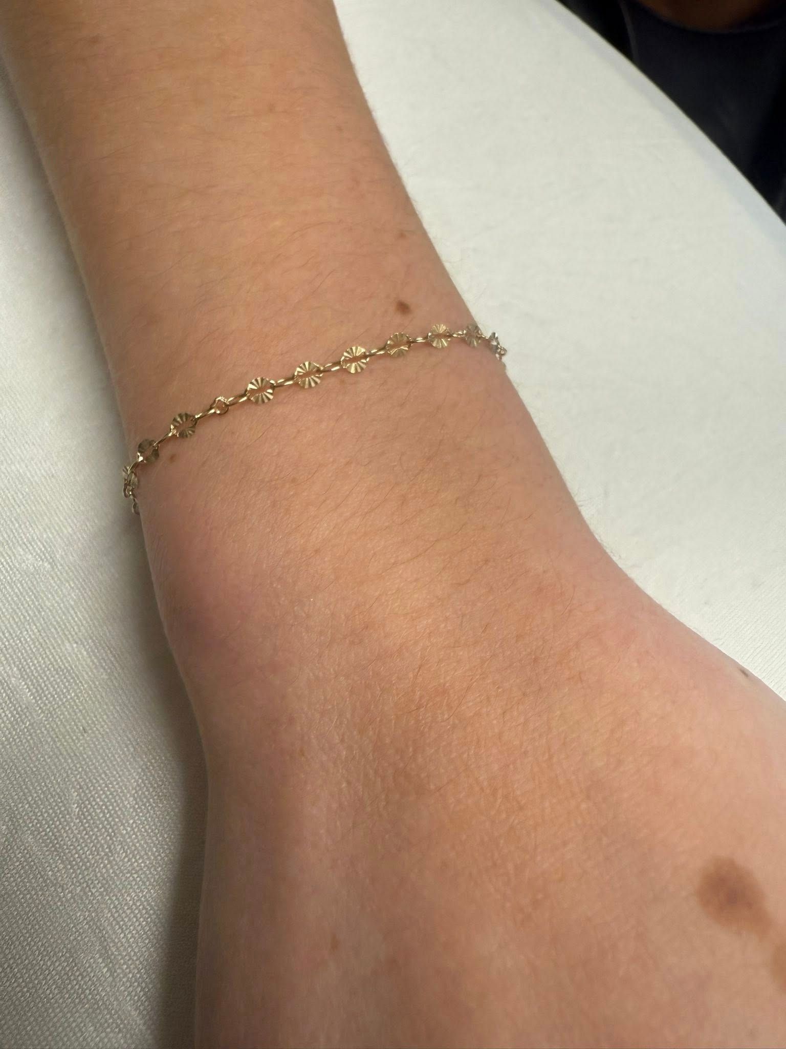 Close-up of a wrist wearing a delicate gold chain bracelet against a light background
