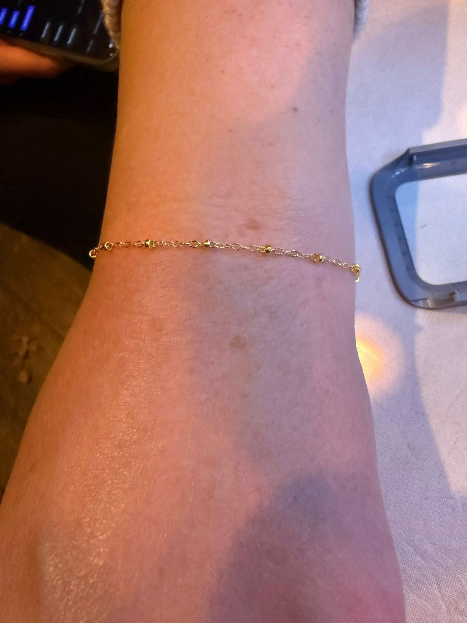 Close-up of a wrist wearing a delicate gold bracelet on a light surface.
