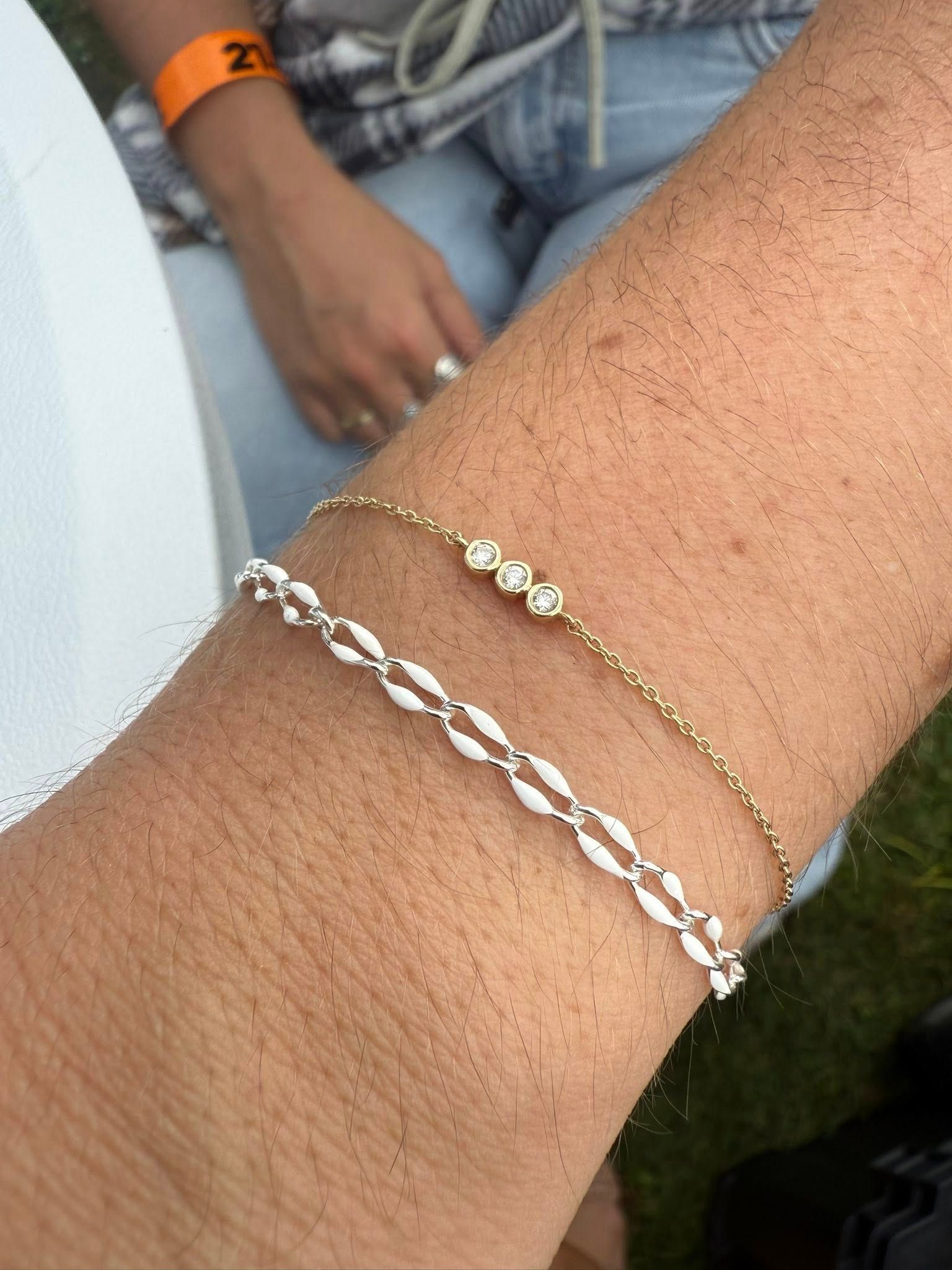Close-up of a wrist wearing silver and gold chain bracelets outdoors.