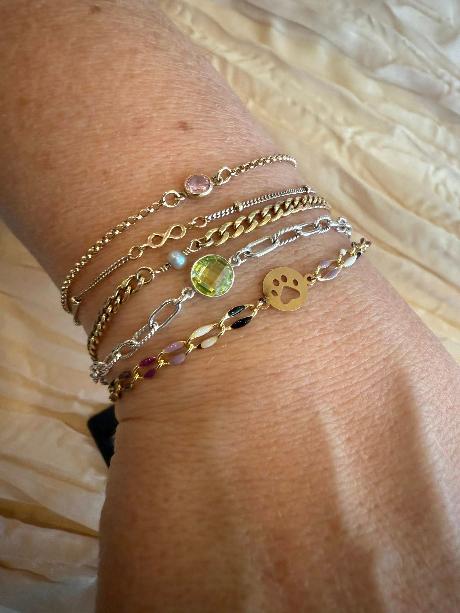Stack of delicate gold bracelets with charms on a wrist over a cream quilted background