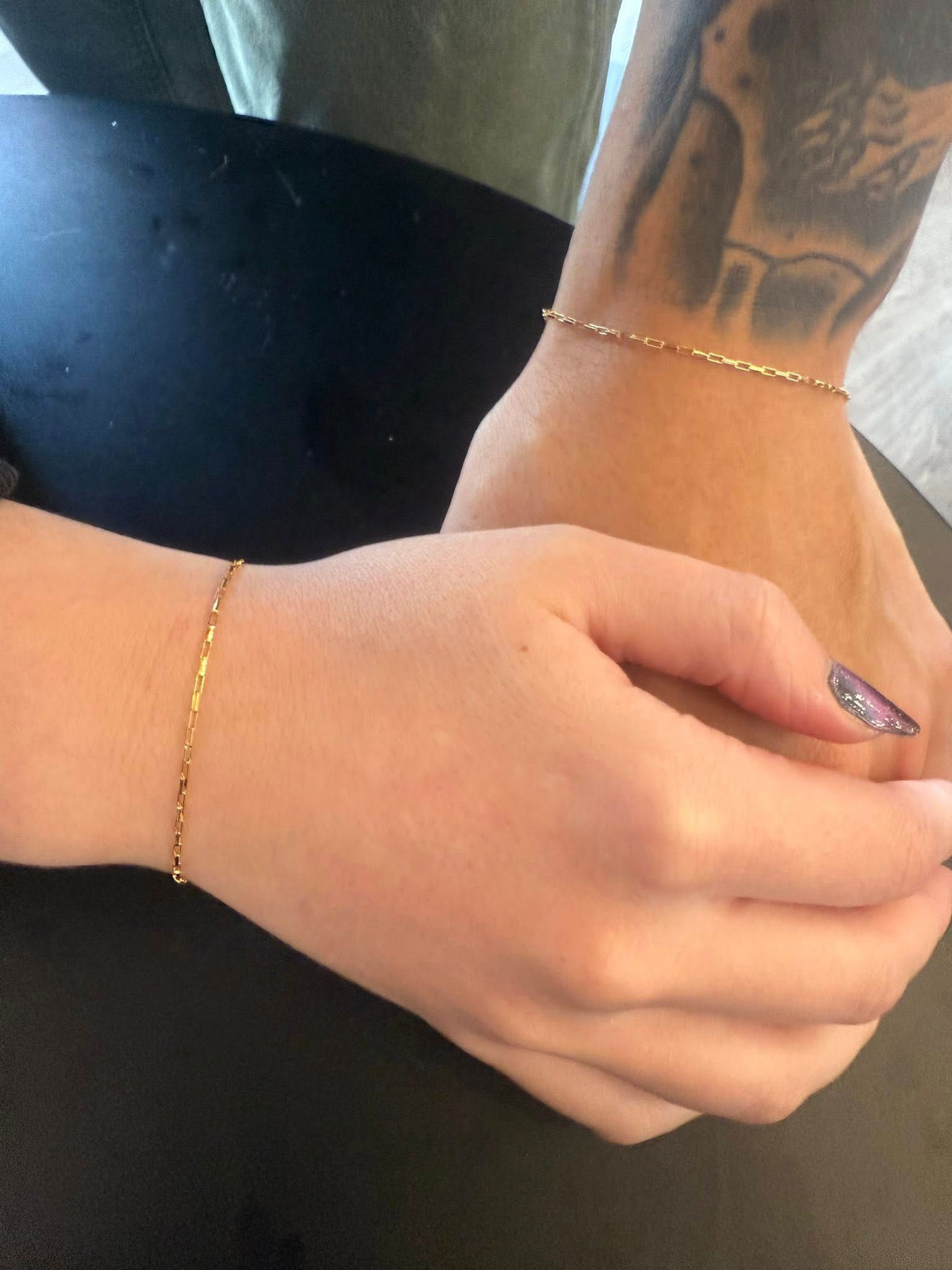 Two clasped hands with gold bracelets and a tattooed forearm resting together