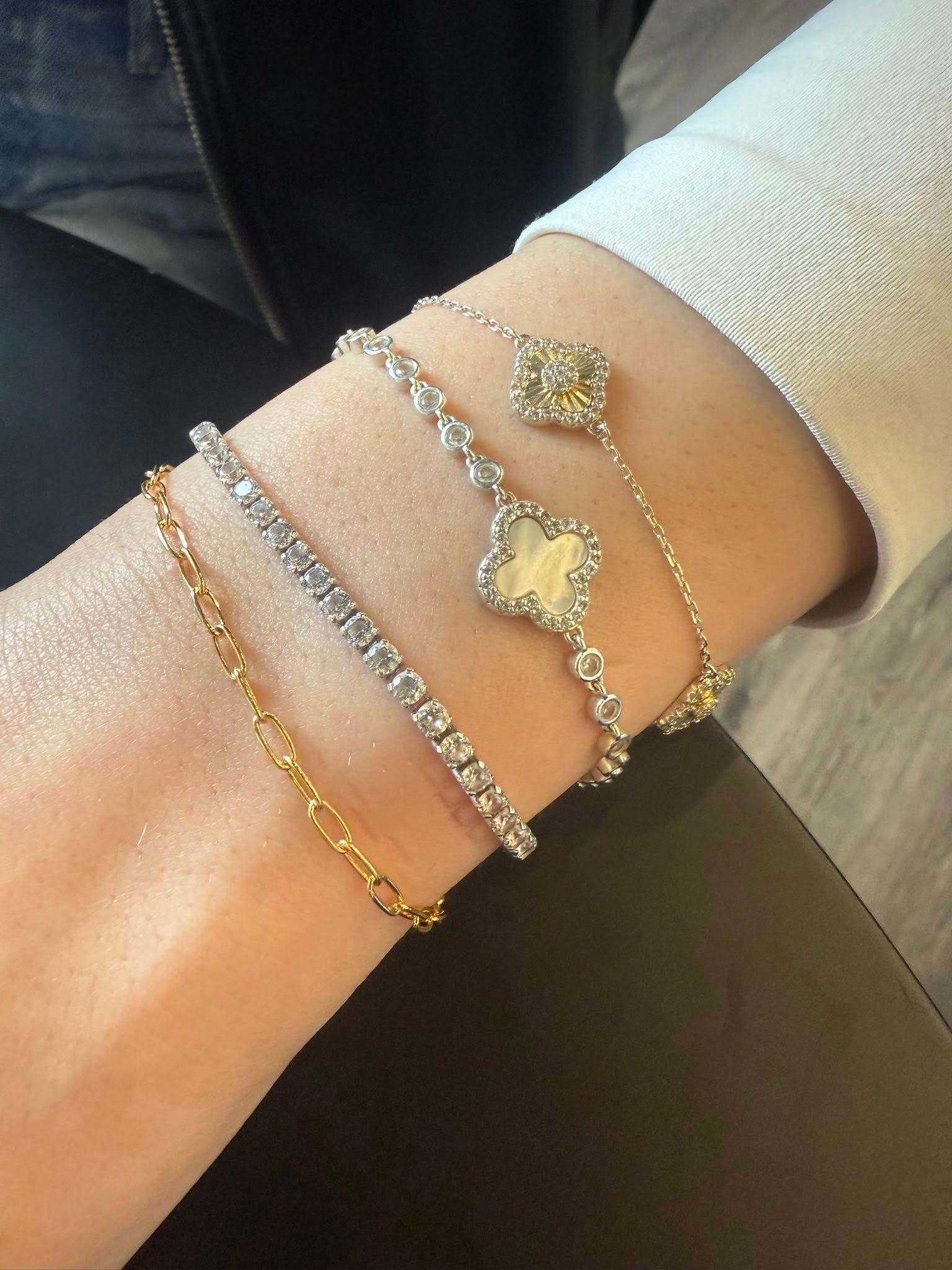 Wrist with four layered bracelets in gold and silver, worn over a cream sweater sleeve.