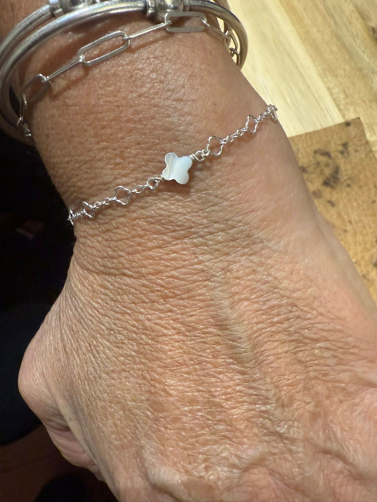 Close-up of a wrist wearing silver chain bracelets, one with a small white charm.