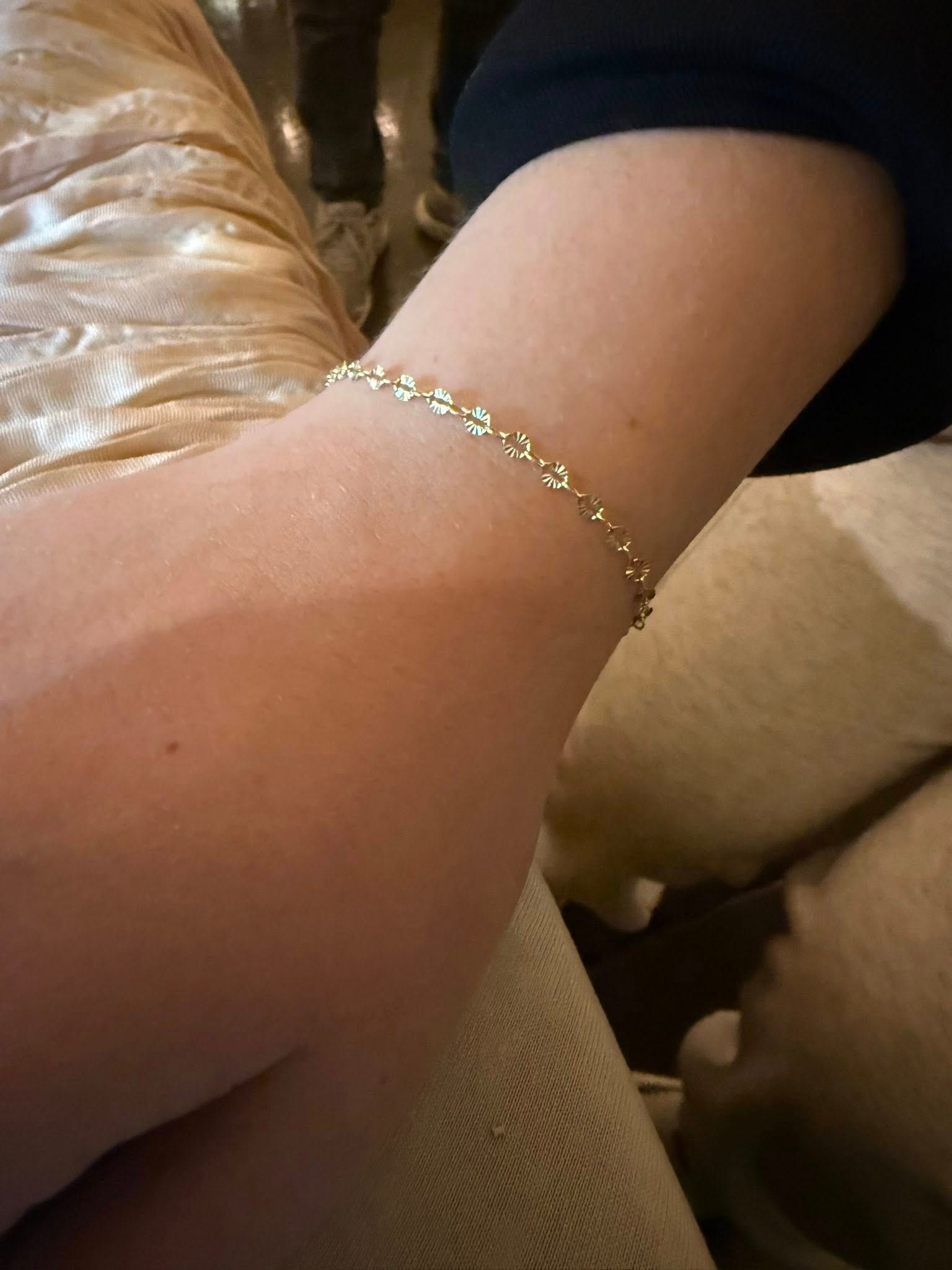 Close-up of an arm wearing a delicate gold bracelet resting on a beige couch.