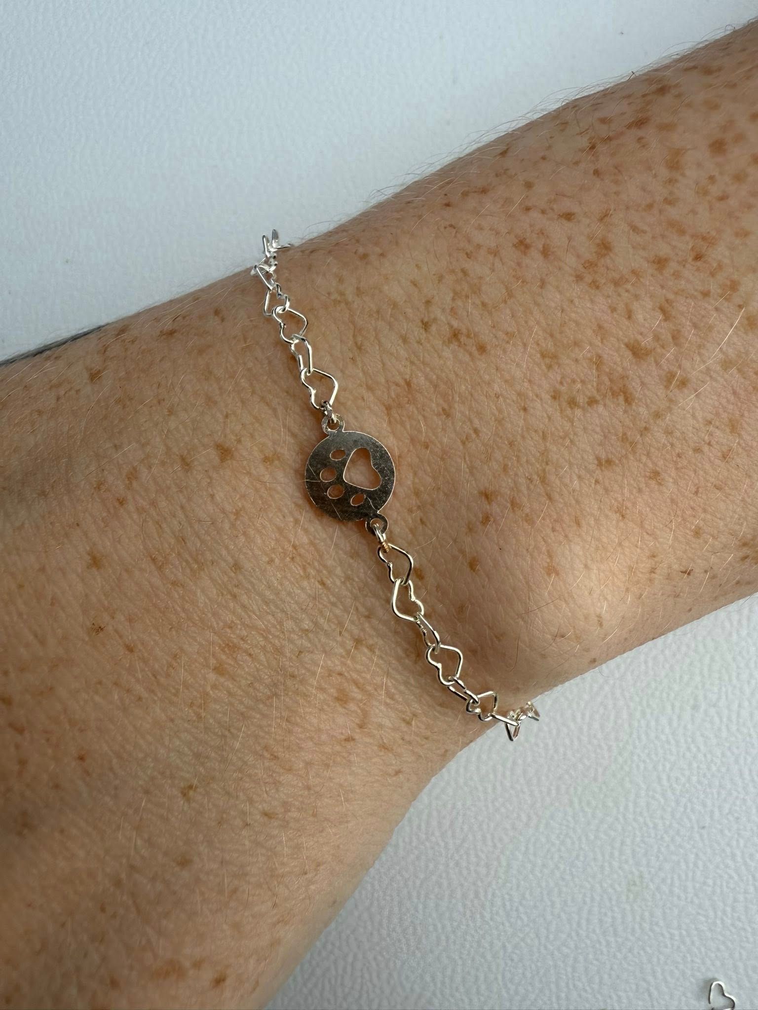 Freckled forearm wearing a delicate silver bracelet with a small round charm