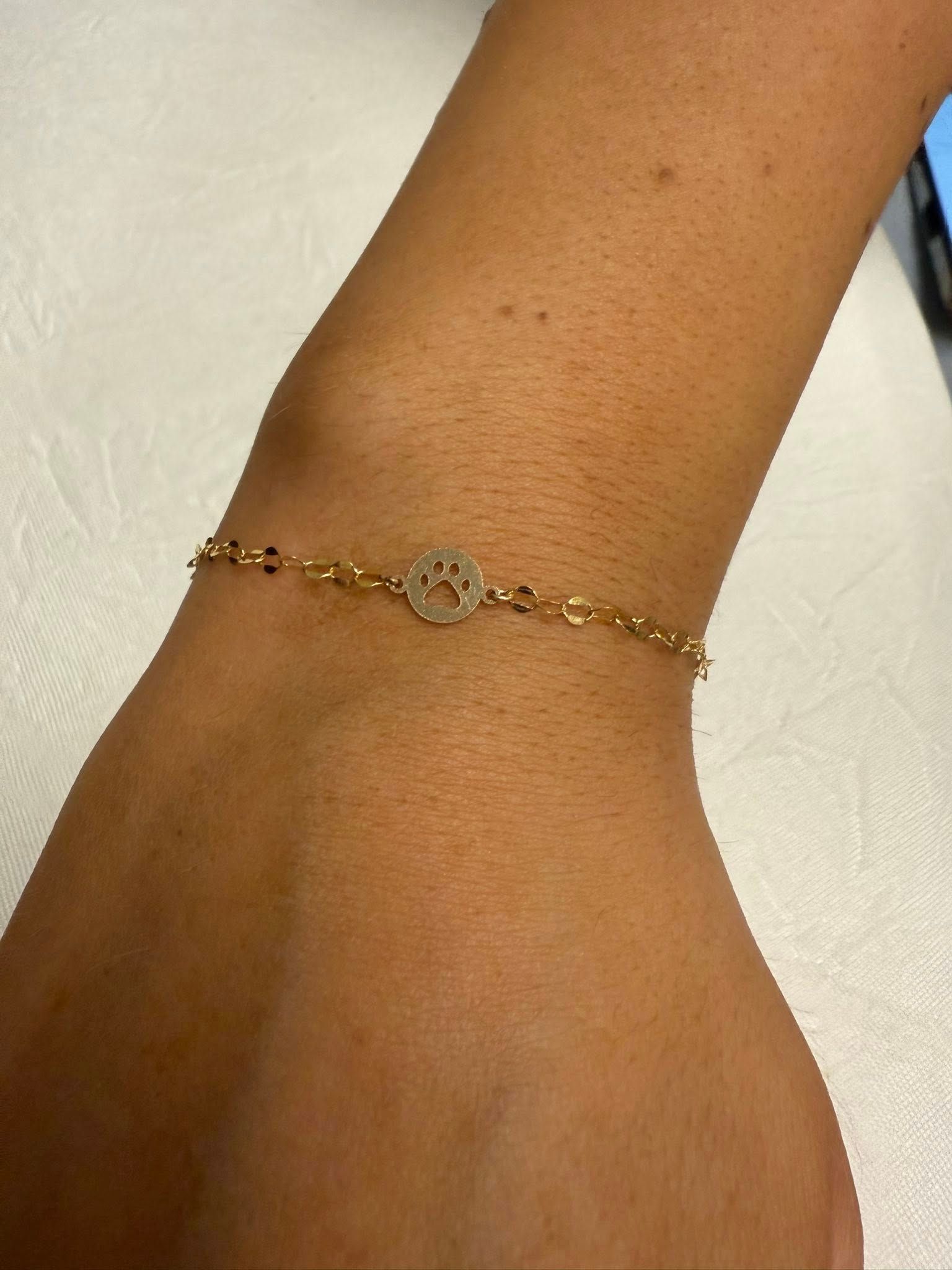 Close-up of an ankle wearing a delicate gold chain bracelet with a small central charm