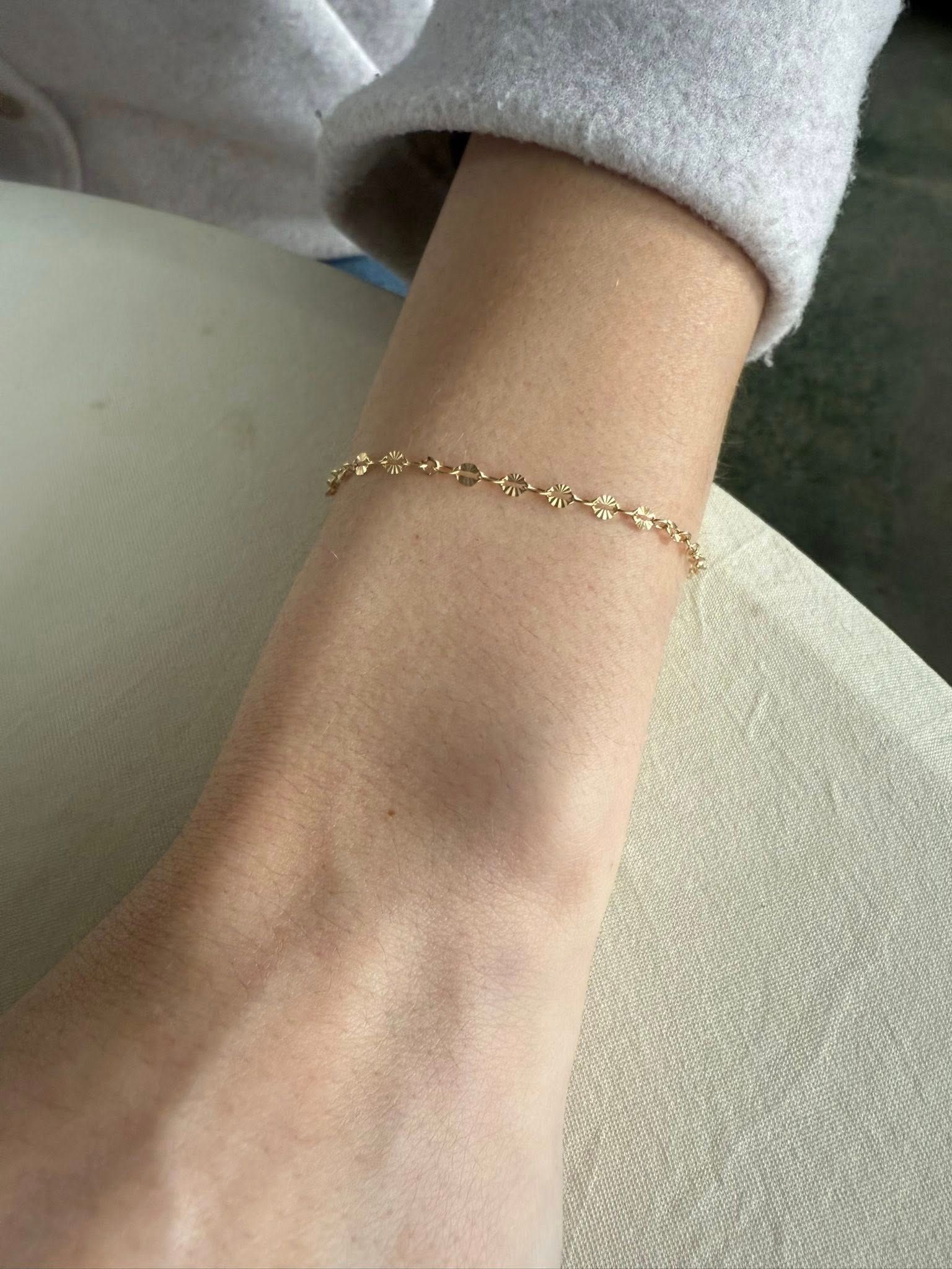 Close-up of a wrist wearing a delicate gold chain bracelet on a light fabric background