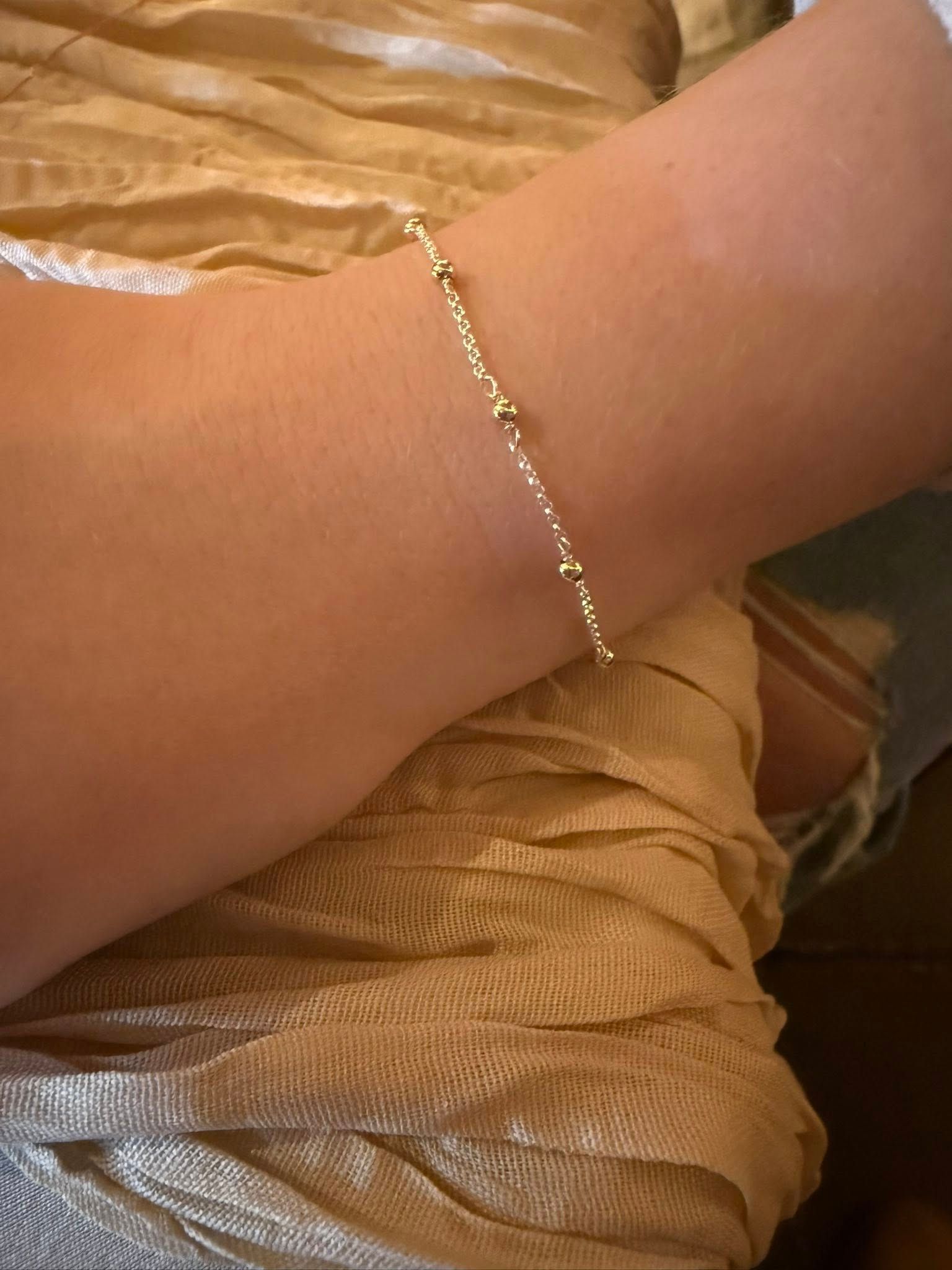 Close-up of a wrist wearing a delicate gold bracelet against a beige fabric background