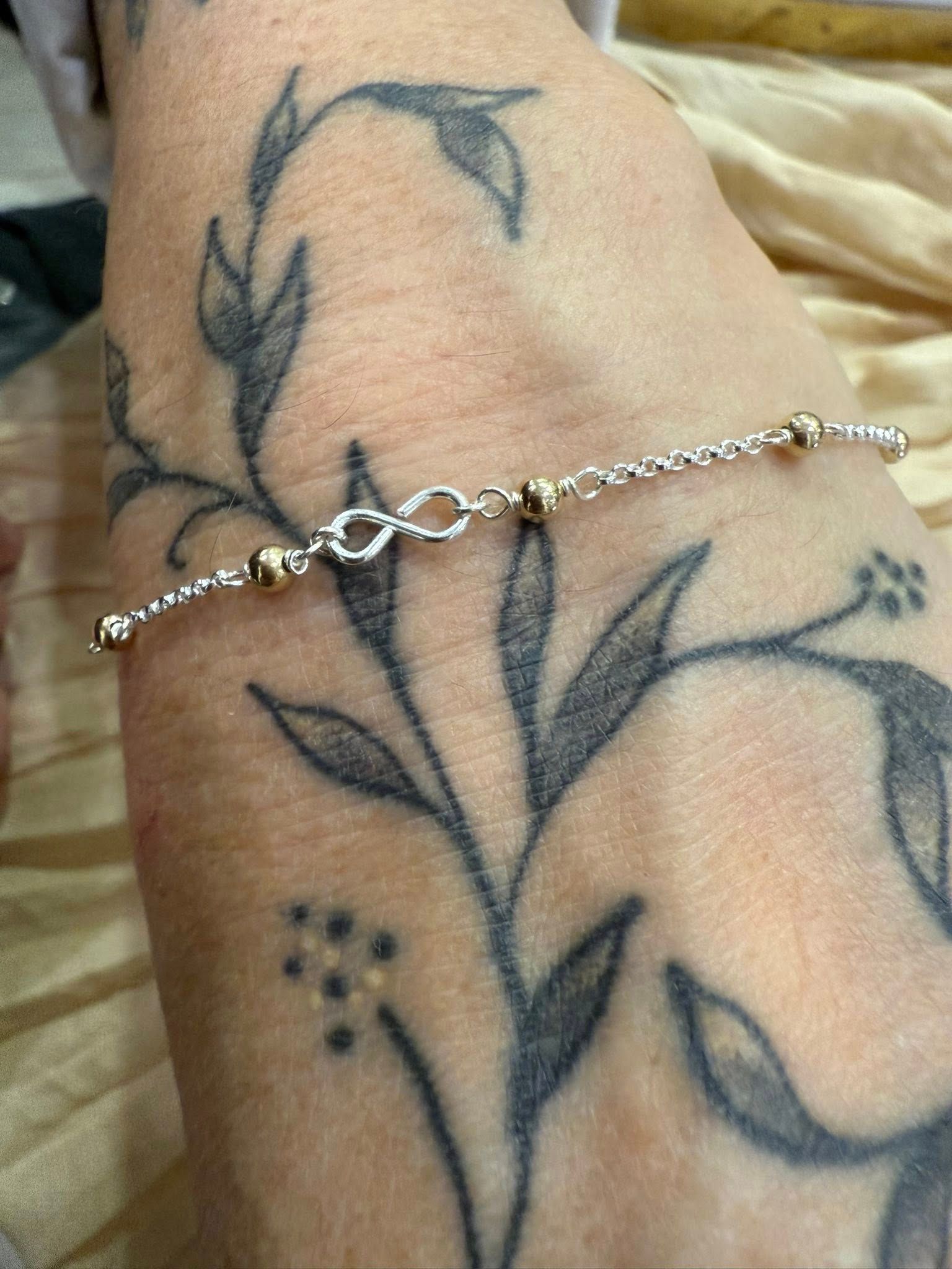 Silver chain bracelet on a wrist with a black floral tattoo.