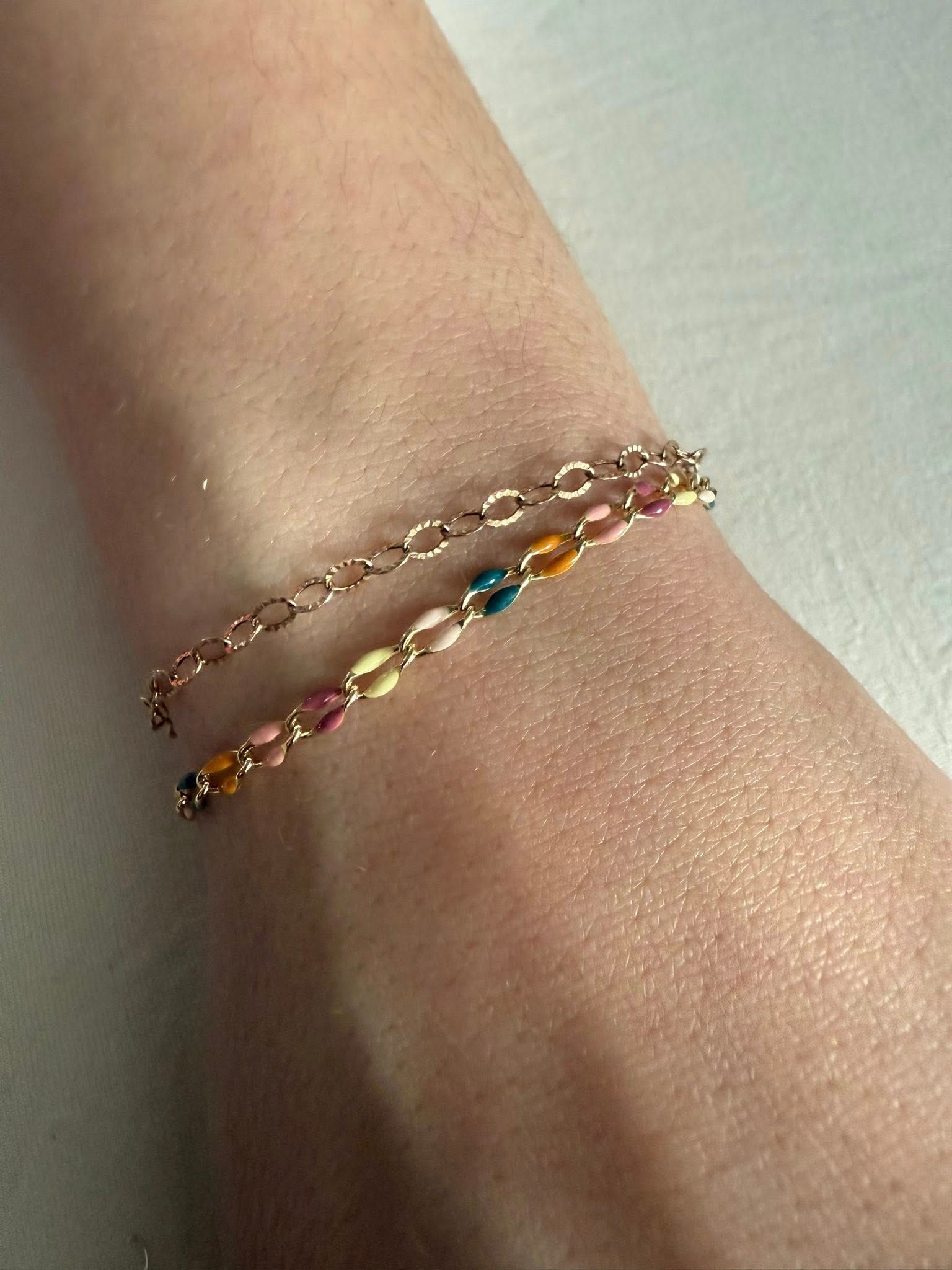 Close-up of a wrist wearing two delicate beaded bracelets, one gold chain and one multicolored strand