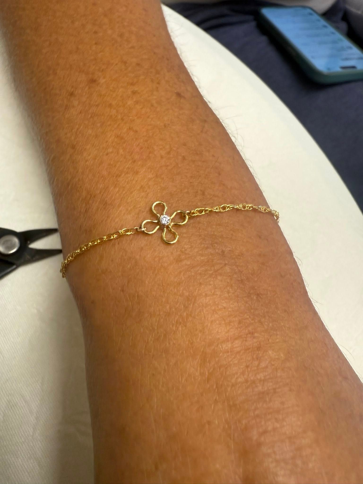 Close-up of a wrist wearing a delicate gold bracelet with a small floral charm